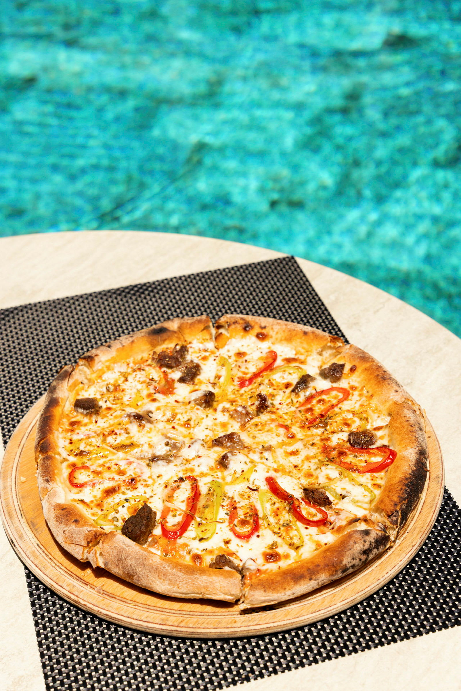 En pizza med fyllning som paprikaskivor och annat är serverad på ett bord med en pool i bakgrunden. (AI-genererad text)