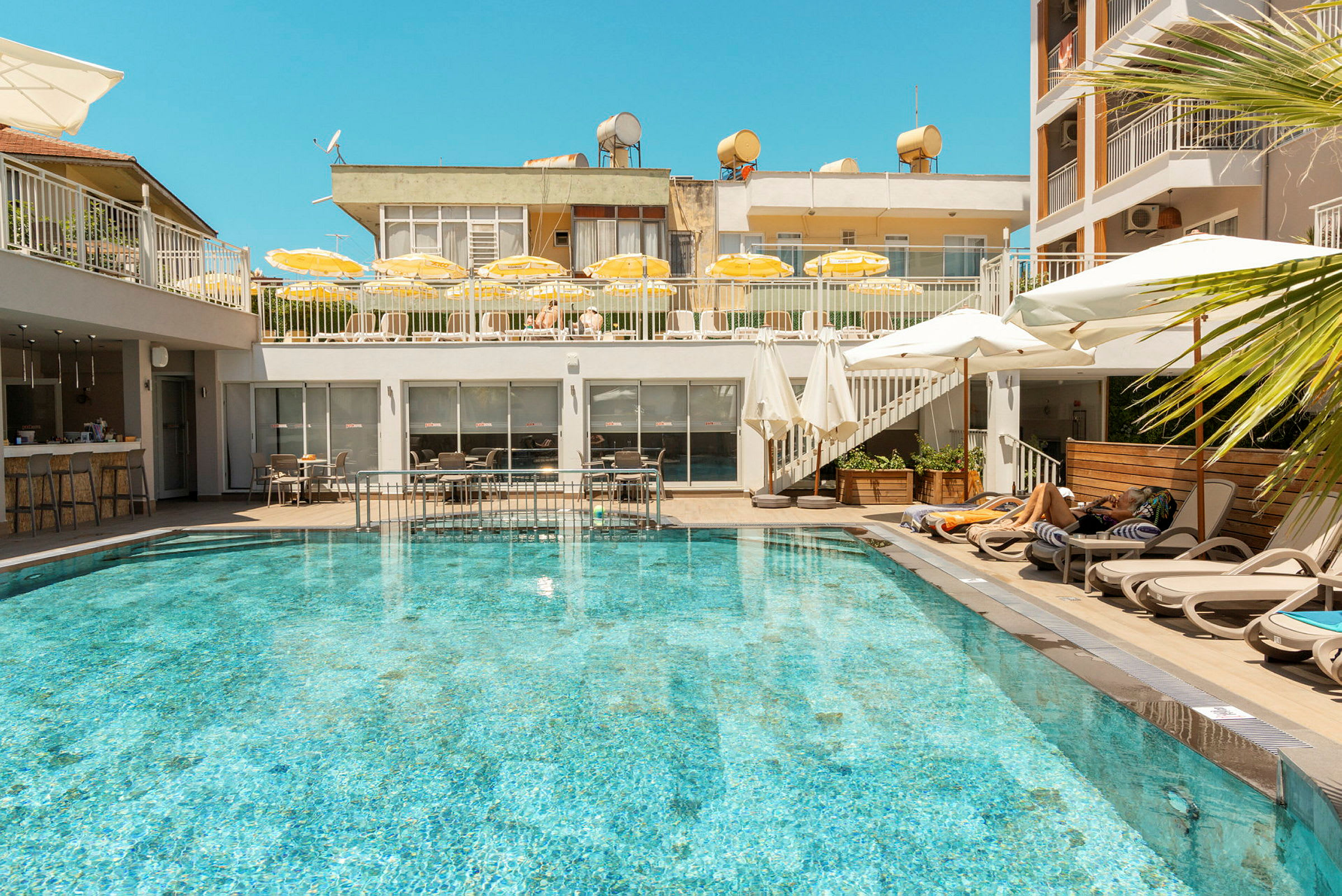 En utomhuspool omgiven av solstolar och parasoller på ett hotell. (AI-genererad text)