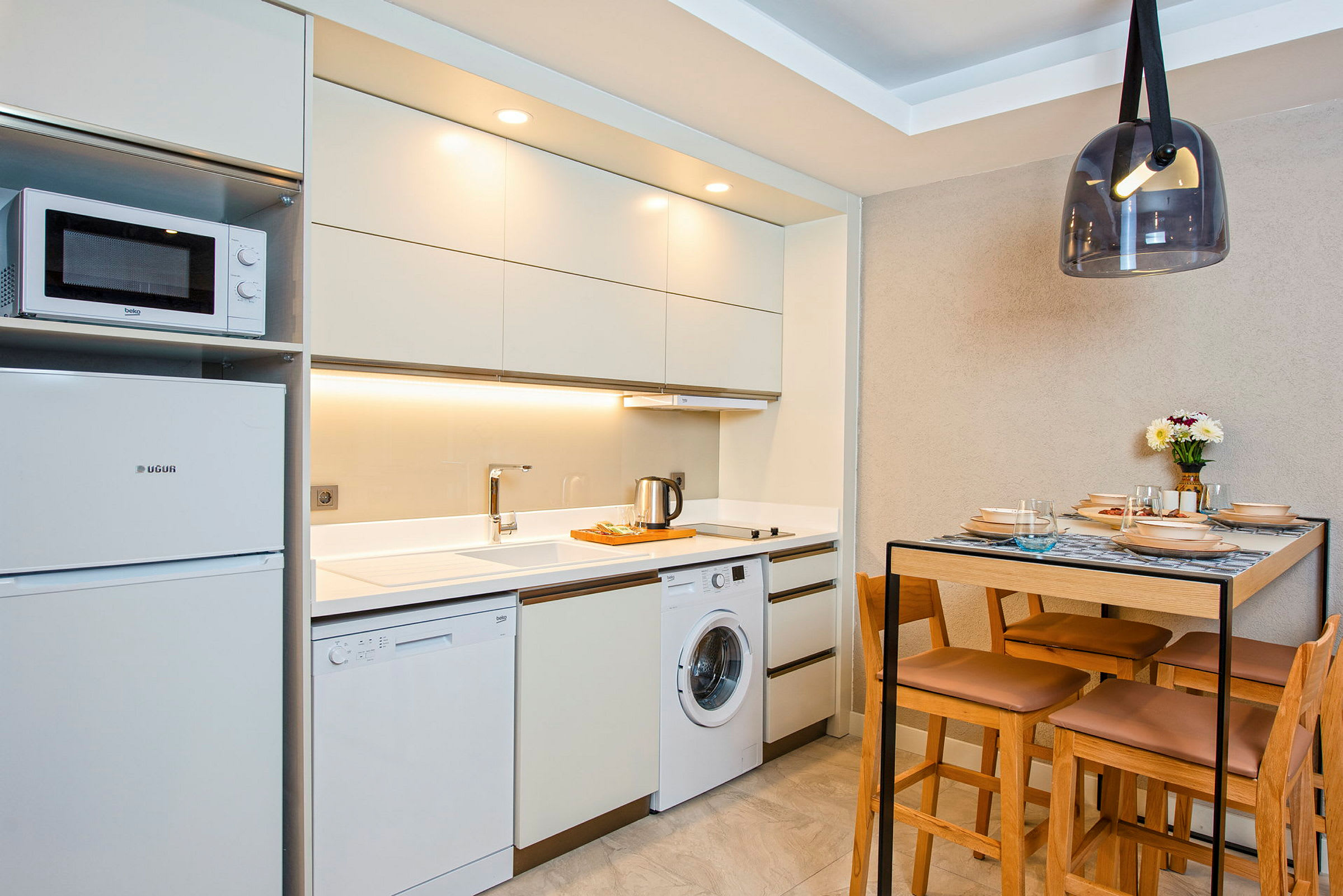 Ett modernt kök med vitrinskåp, diskho, tvättmaskin, diskmaskin och en matplats med ett bord och stolar. (AI-genererad text)