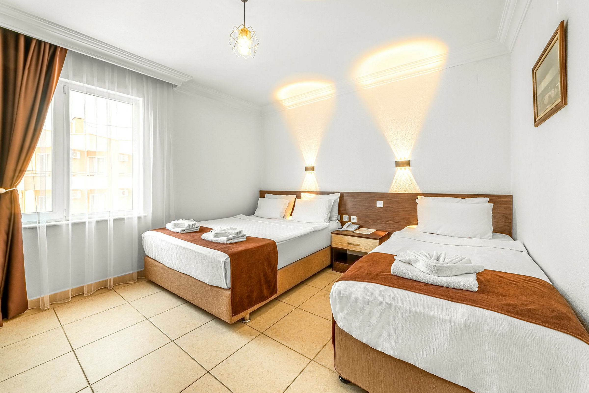 Hotellrum med två separata sängar, ljus insredning och en fönster med mörka gardiner. (AI-genererad text)