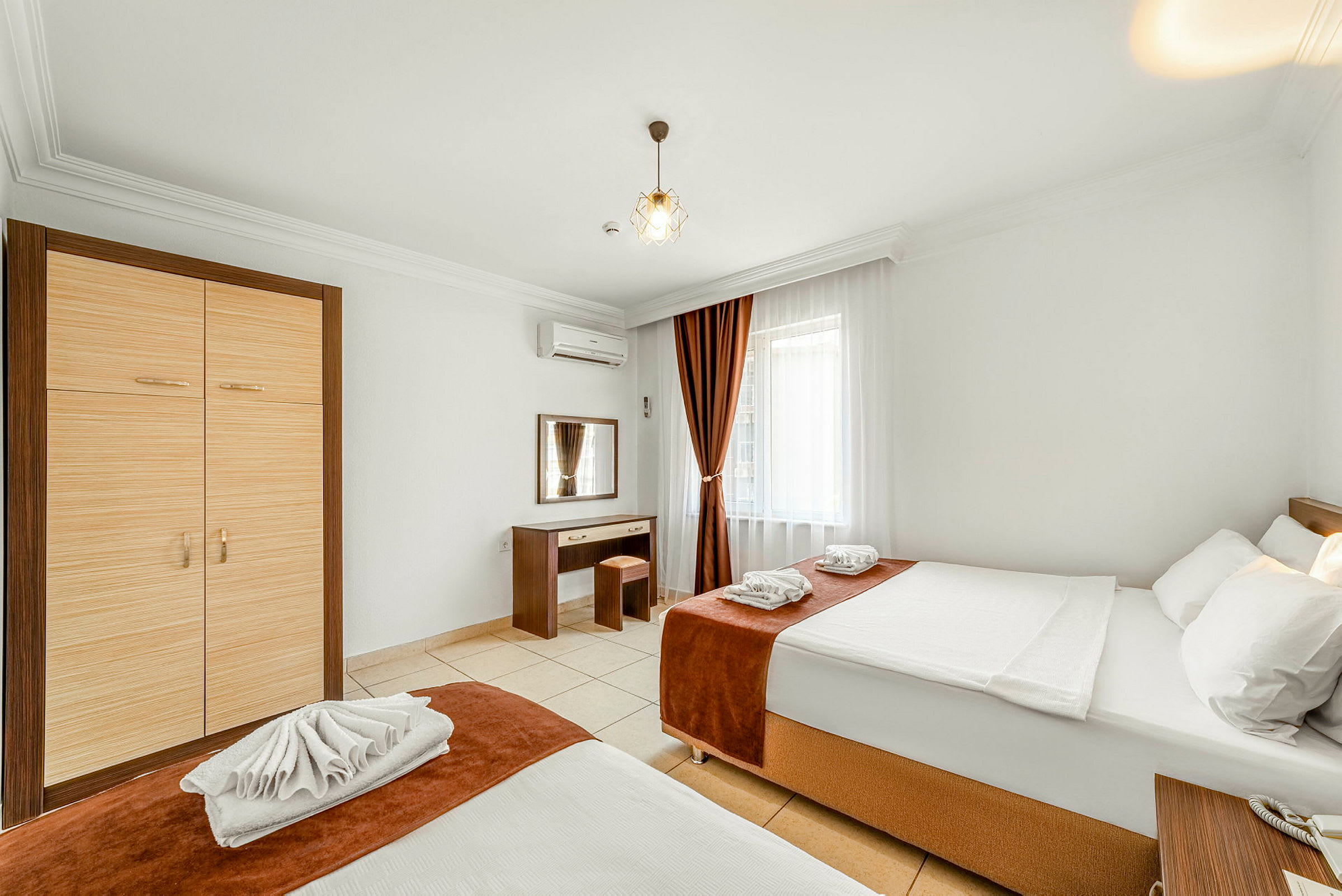 Ett hotellrum med två sängar, en garderob, ett skrivbord och ett fönster med gardiner. (AI-genererad text)