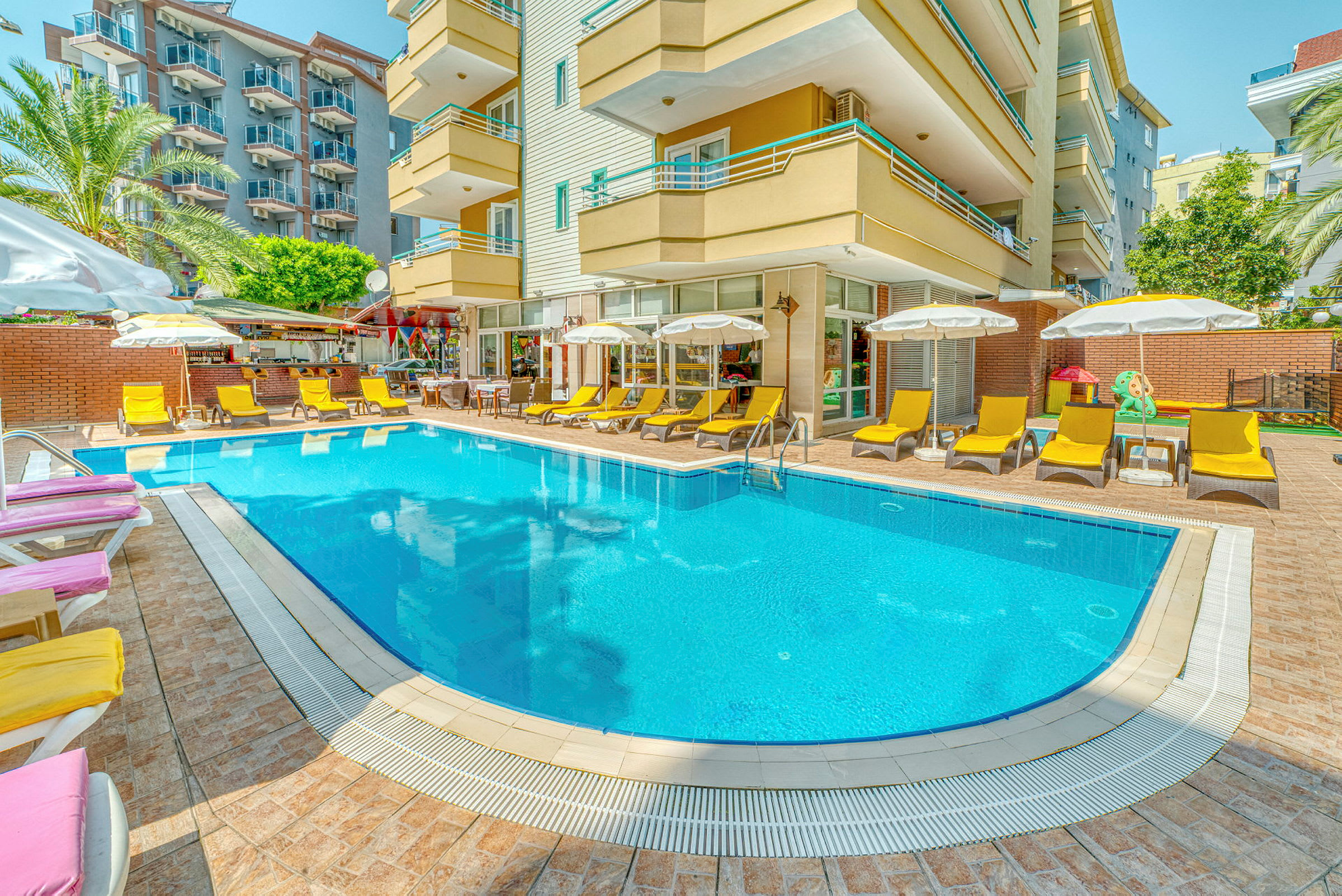 En utomhuspool omgiven av solstolar och parasoller framför en hotellbyggnad. (AI-genererad text)