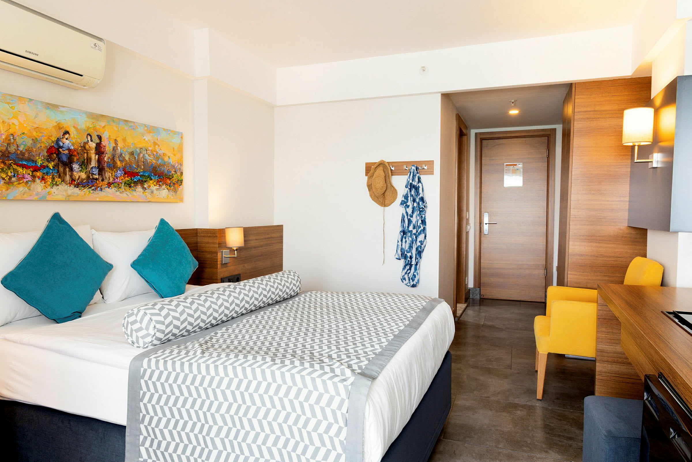 Ett hotellrum med en säng, blå kuddar och en målning på väggen. (AI-genererad text)