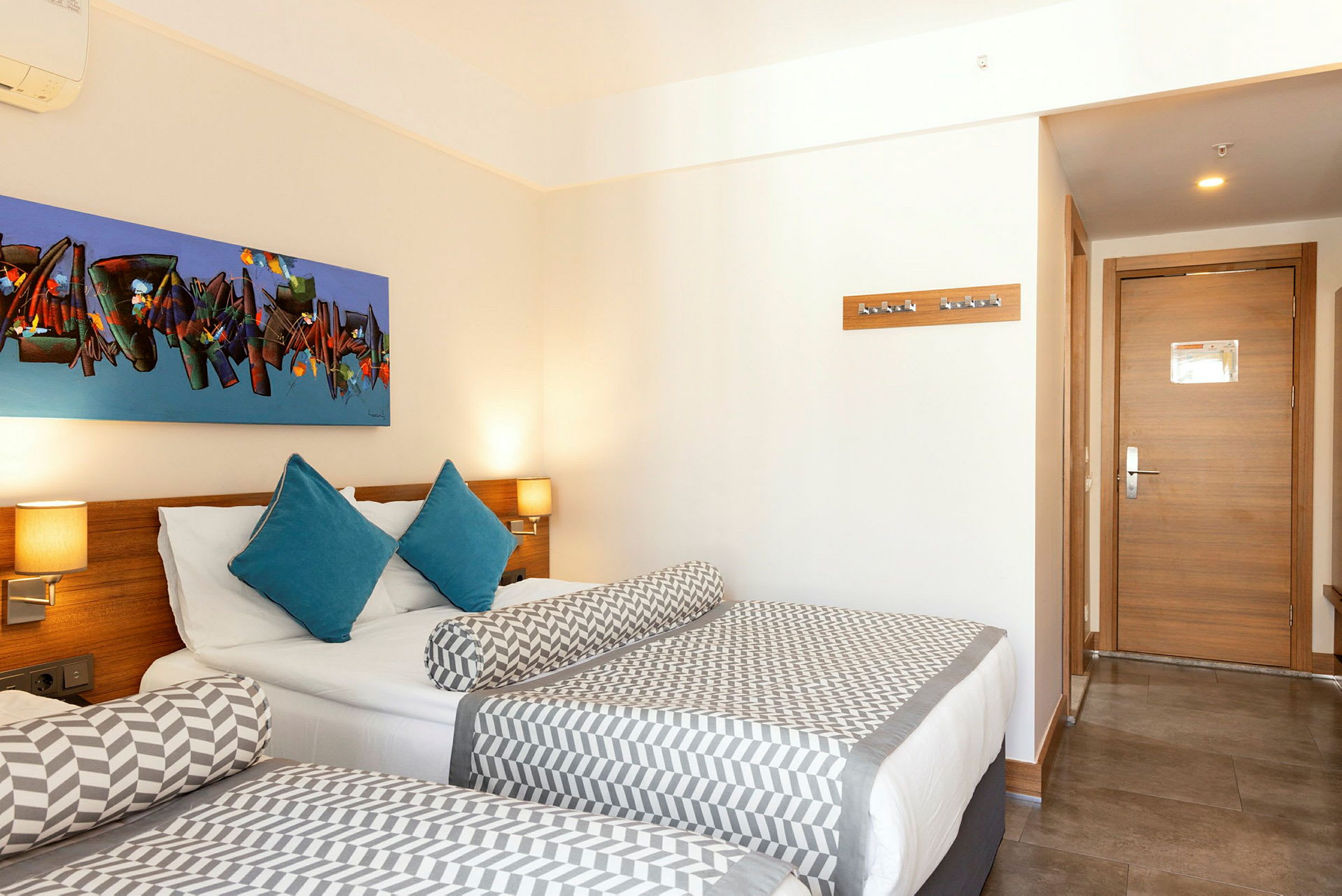 Hotellrum med två sängar, ett färgglatt konstverk ovanför sängen och en ingångsdörr. (AI-genererad text)