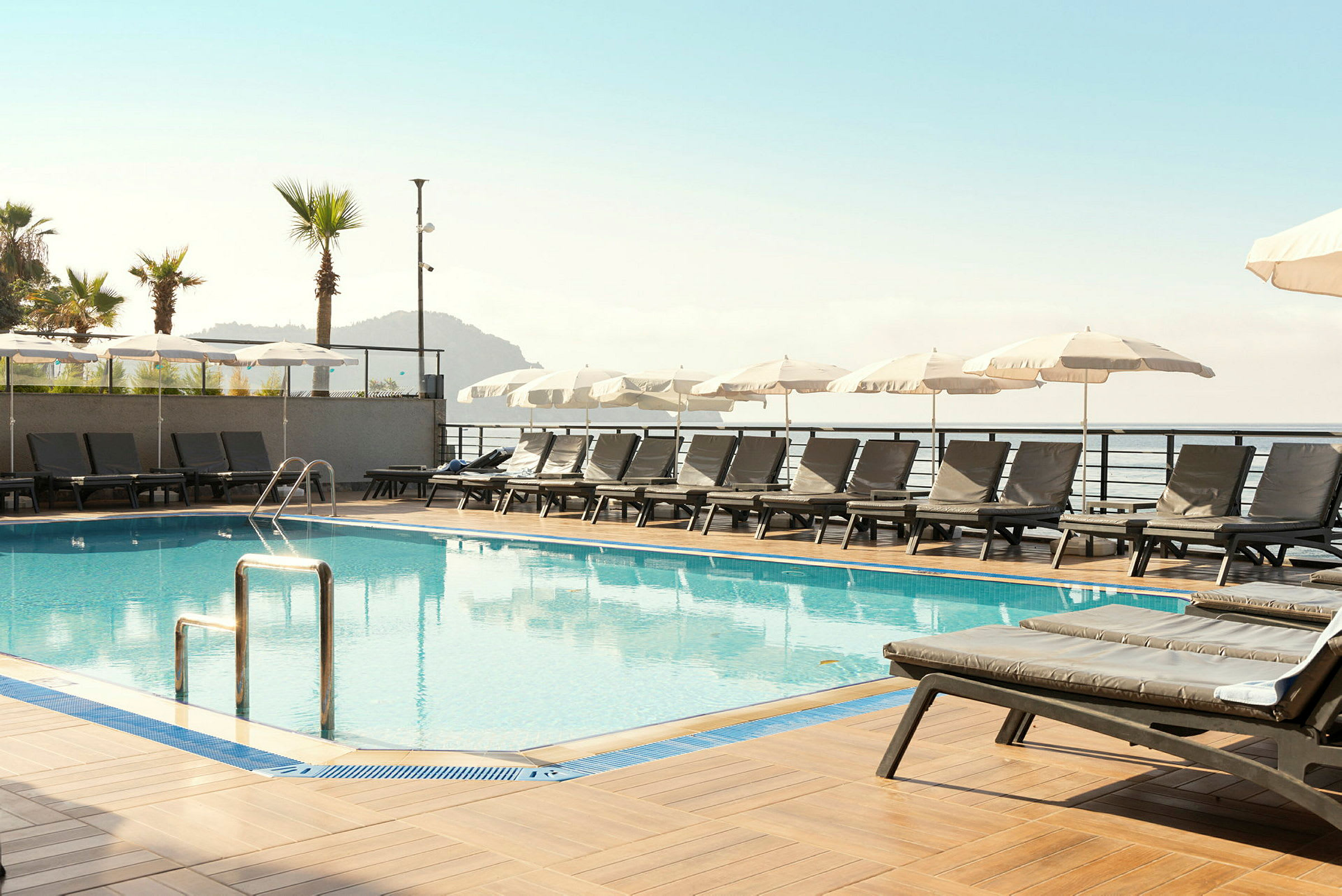 Utsikt över en pool med solstolar och parasoller vid sidan, samt hav i bakgrunden. (AI-genererad text)