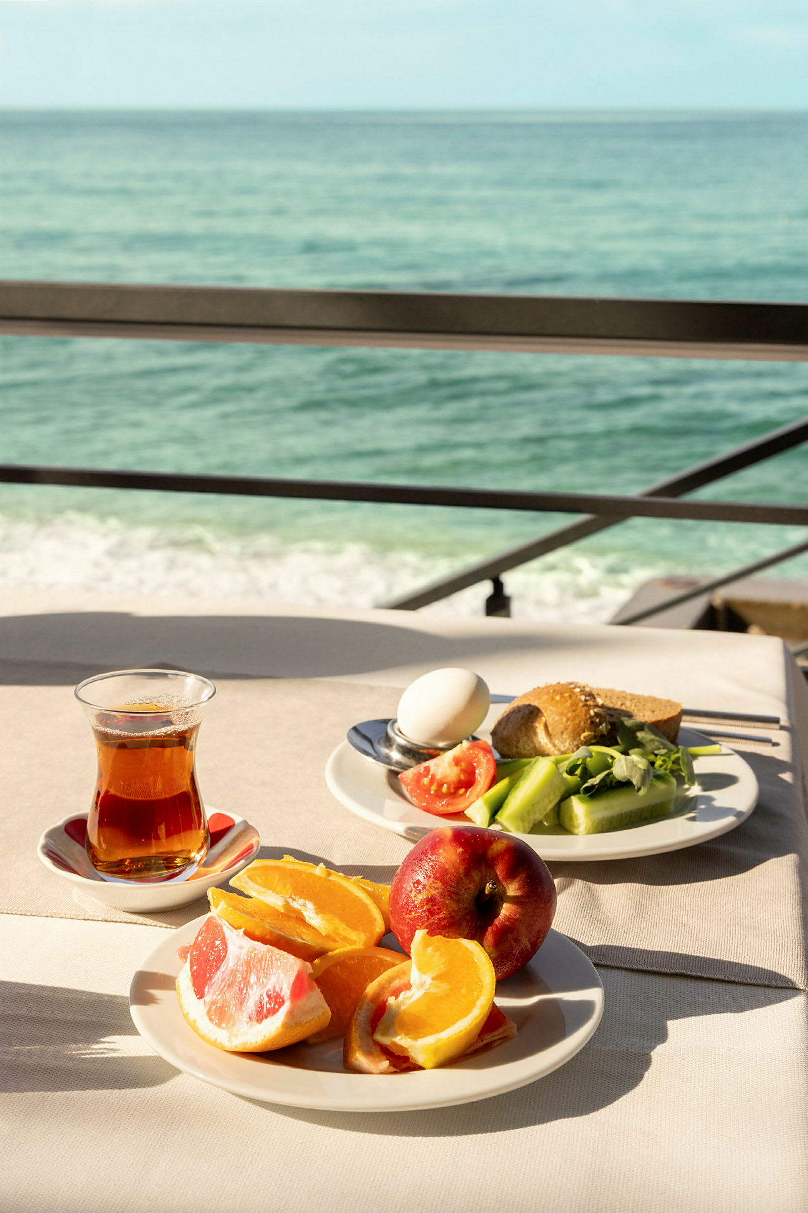 Frukost med havsutsikt, inklusive apelsinklyftor, grapefrukt, äpple, te och sallad. (AI-genererad text)