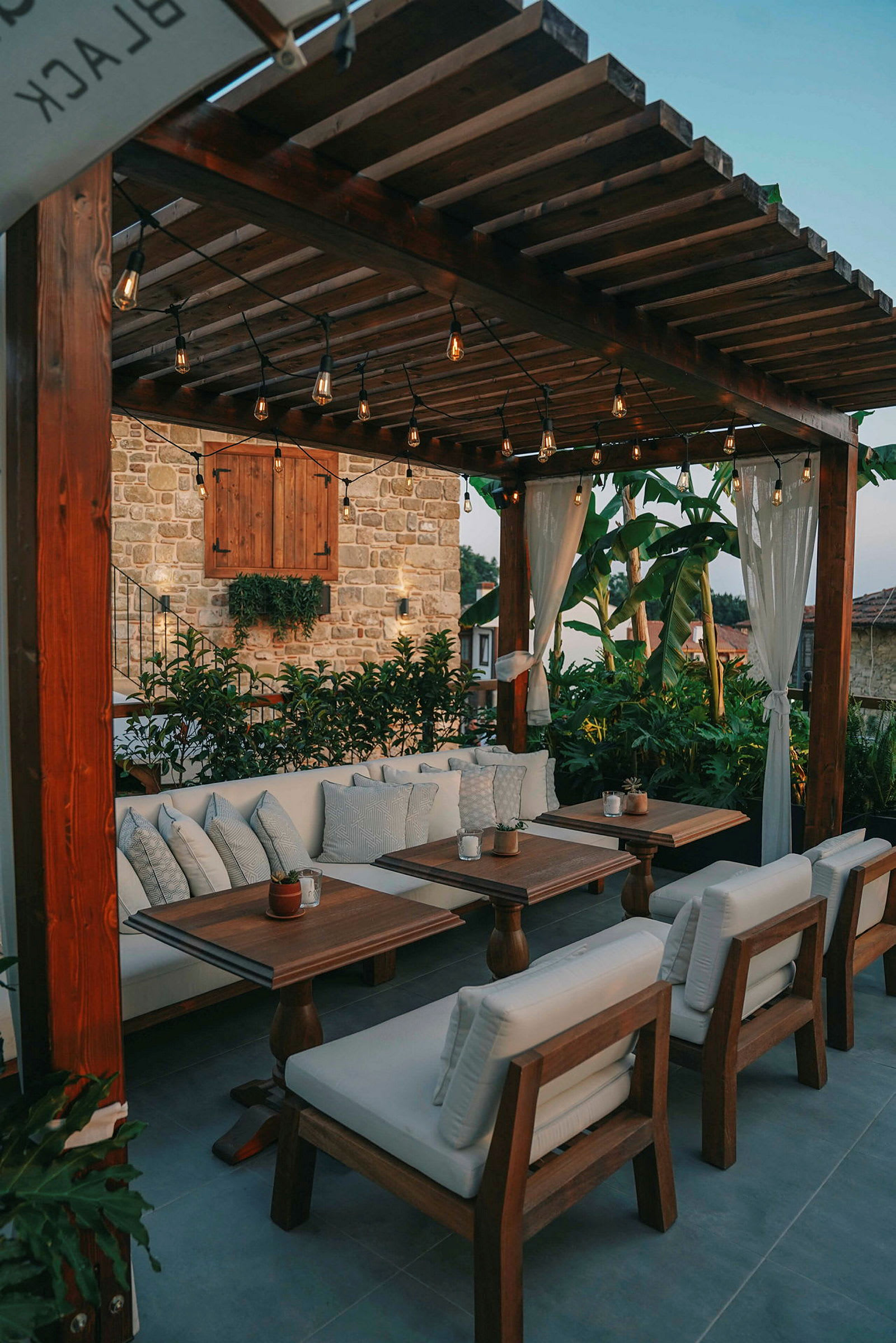 Utomhus lounge med träbord och vita kuddar under pergola. (AI-genererad text)