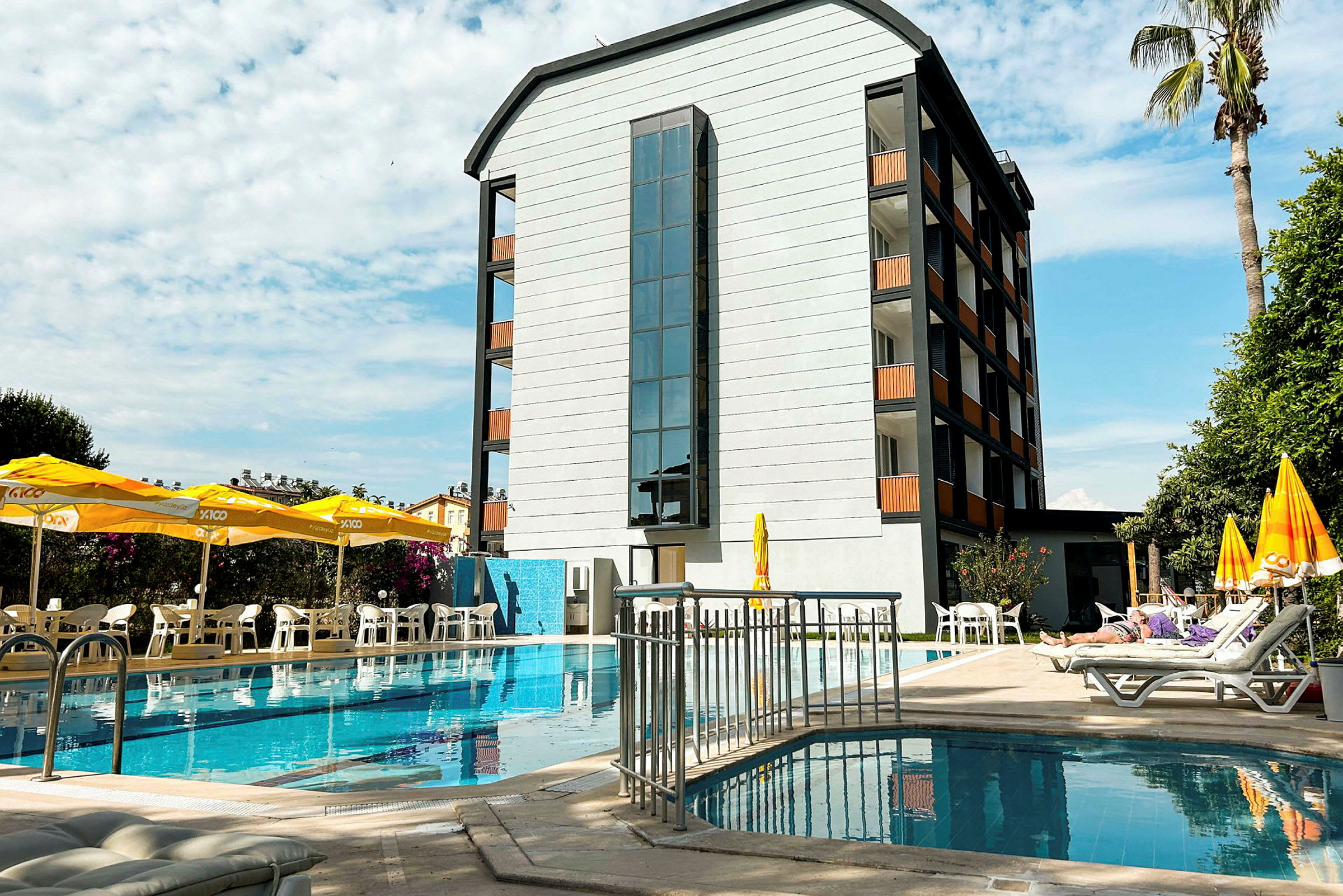 En byggnad vid en pool med solstolar och parasoller på terrassen. (AI-genererad text)