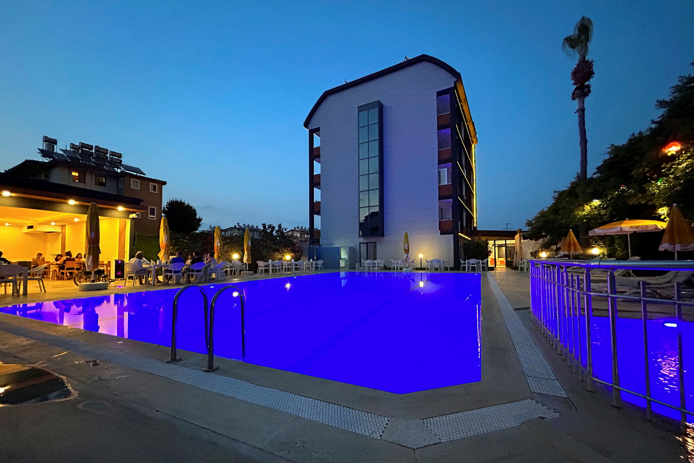 En hotellbyggnad med en upplyst pool framför som omges av stolar och parasoller vid skymning. (AI-genererad text)