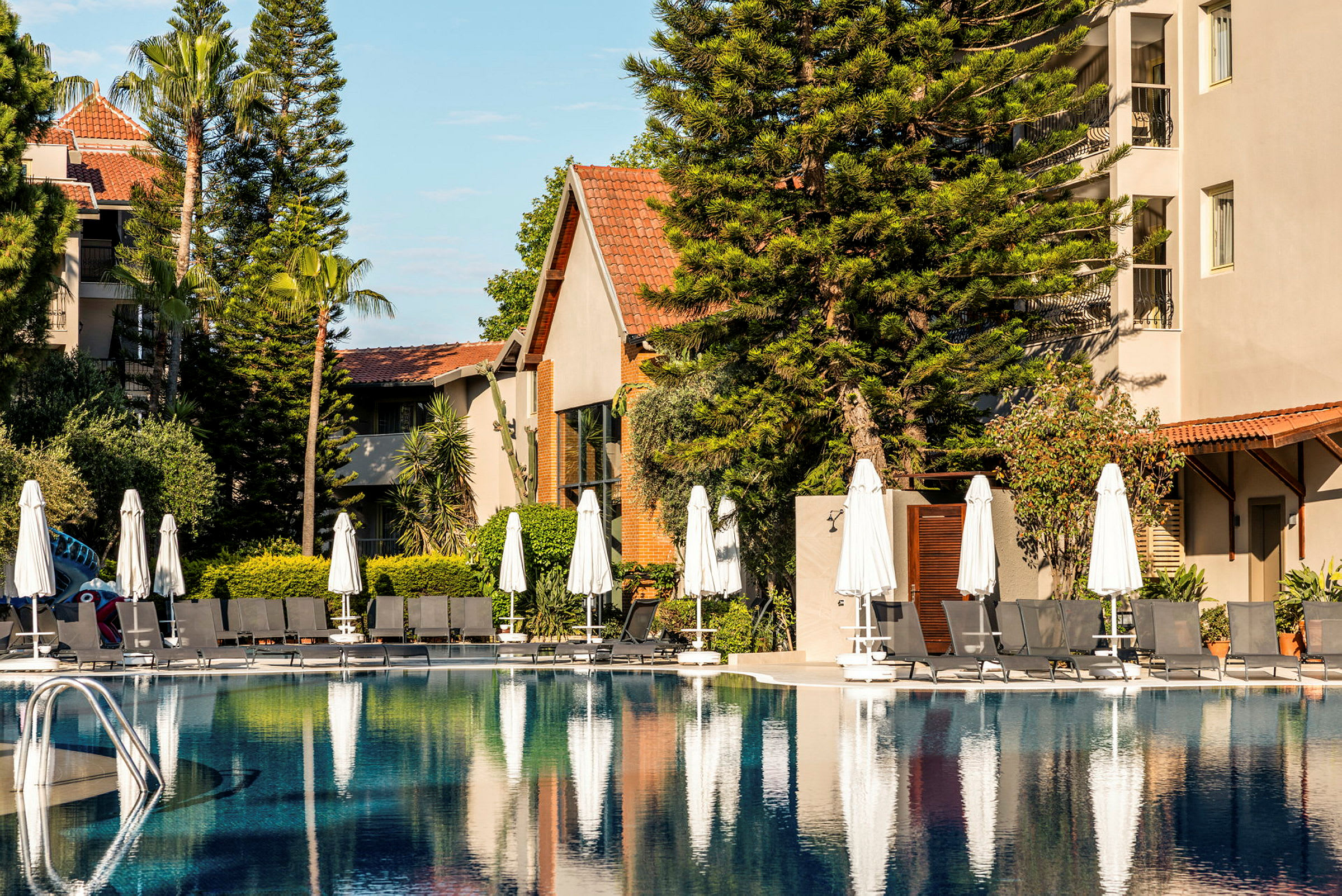 Bild av en pool vid ett hotell, omgiven av solstolar, parasoller och grönska. (AI-genererad text)