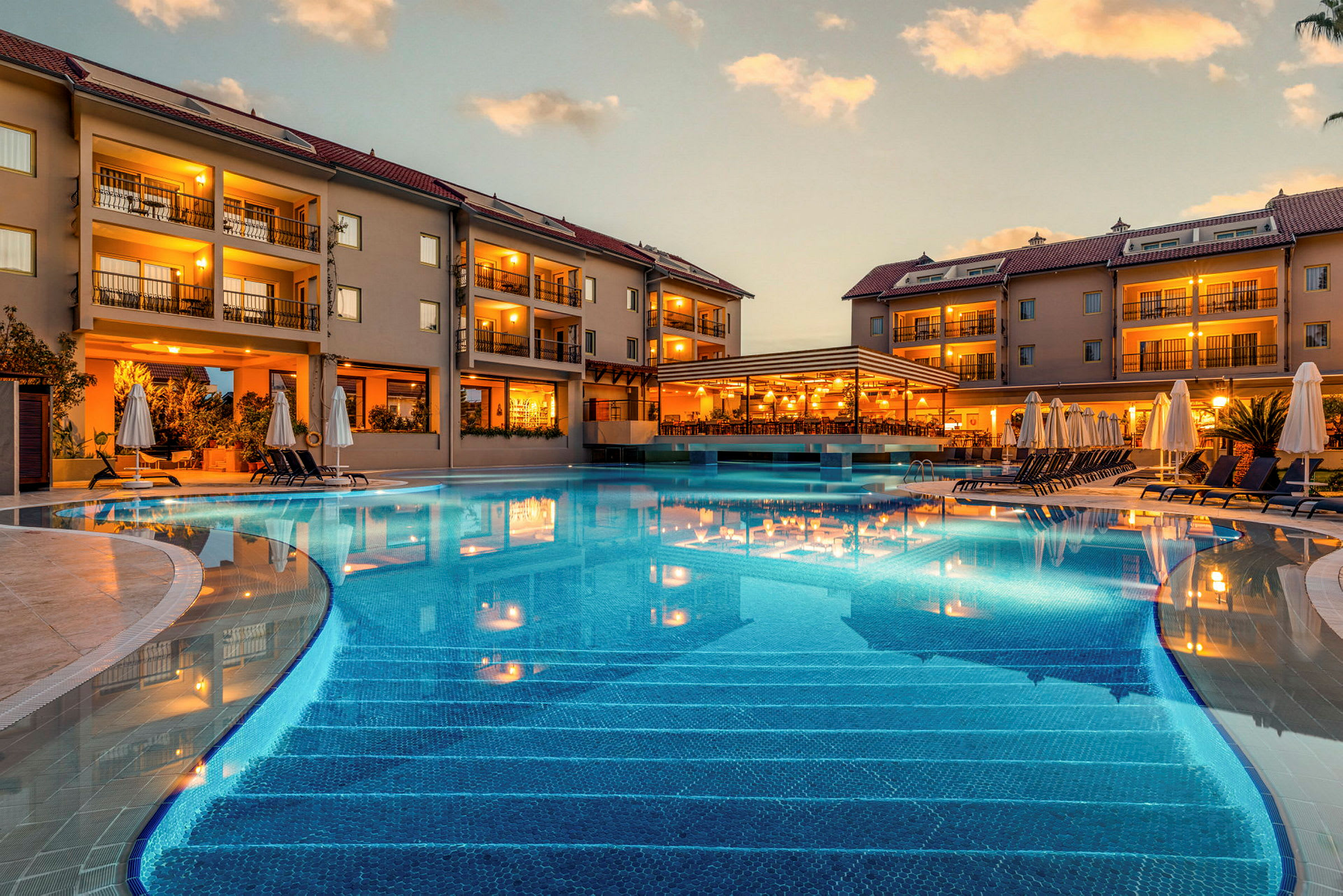 Hotellkomplex med pool och solstolar vid skymning. (AI-genererad text)