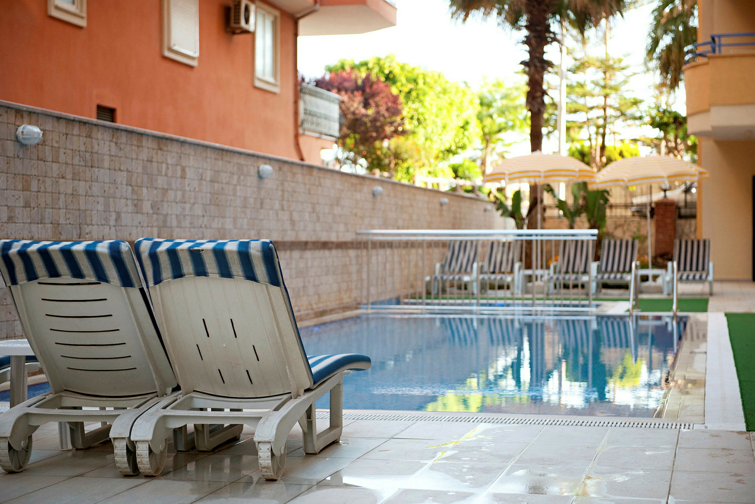 Två solstolar vid kanten av en pool, med parasoll och fler solstolar i bakgrunden. (AI-genererad text)
