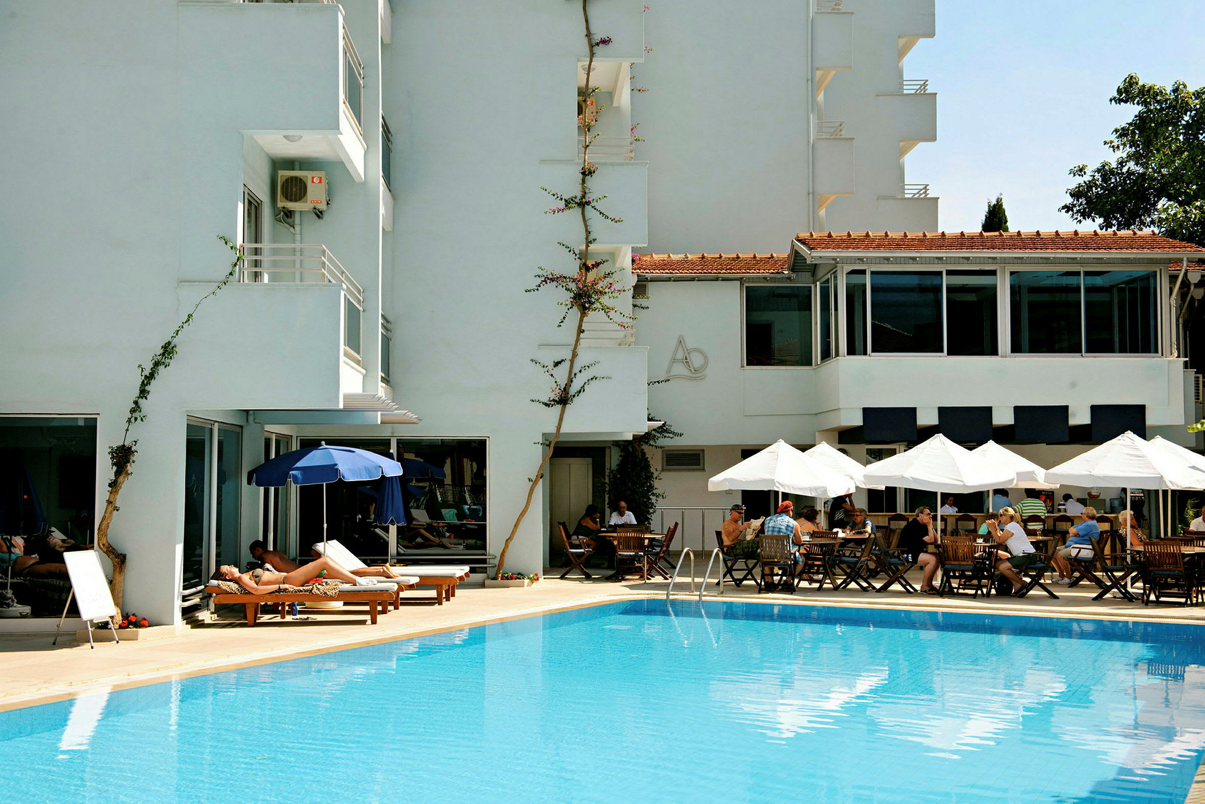 En pool framför ett hotell med solstolar och bord under parasoller. (AI-genererad text)