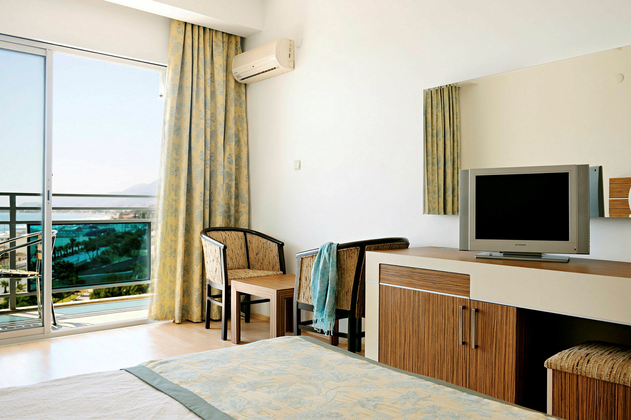 Ett hotellrum med en TV, två stolar och ett bord bredvid en glasdörr som leder ut till en balkong. (AI-genererad text)