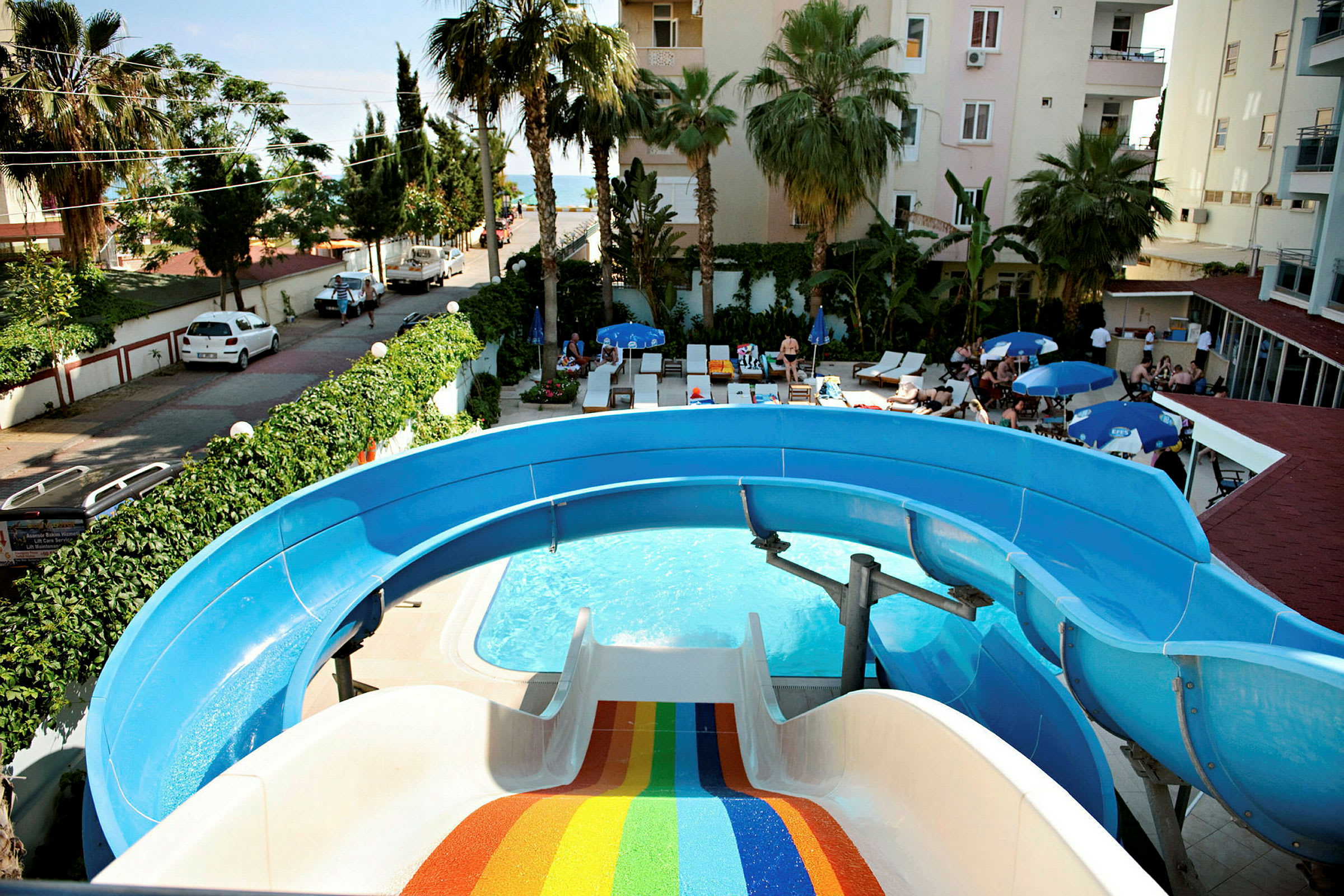 En pool med vattenrutschbana och solstolar i en hotellträdgård. (AI-genererad text)
