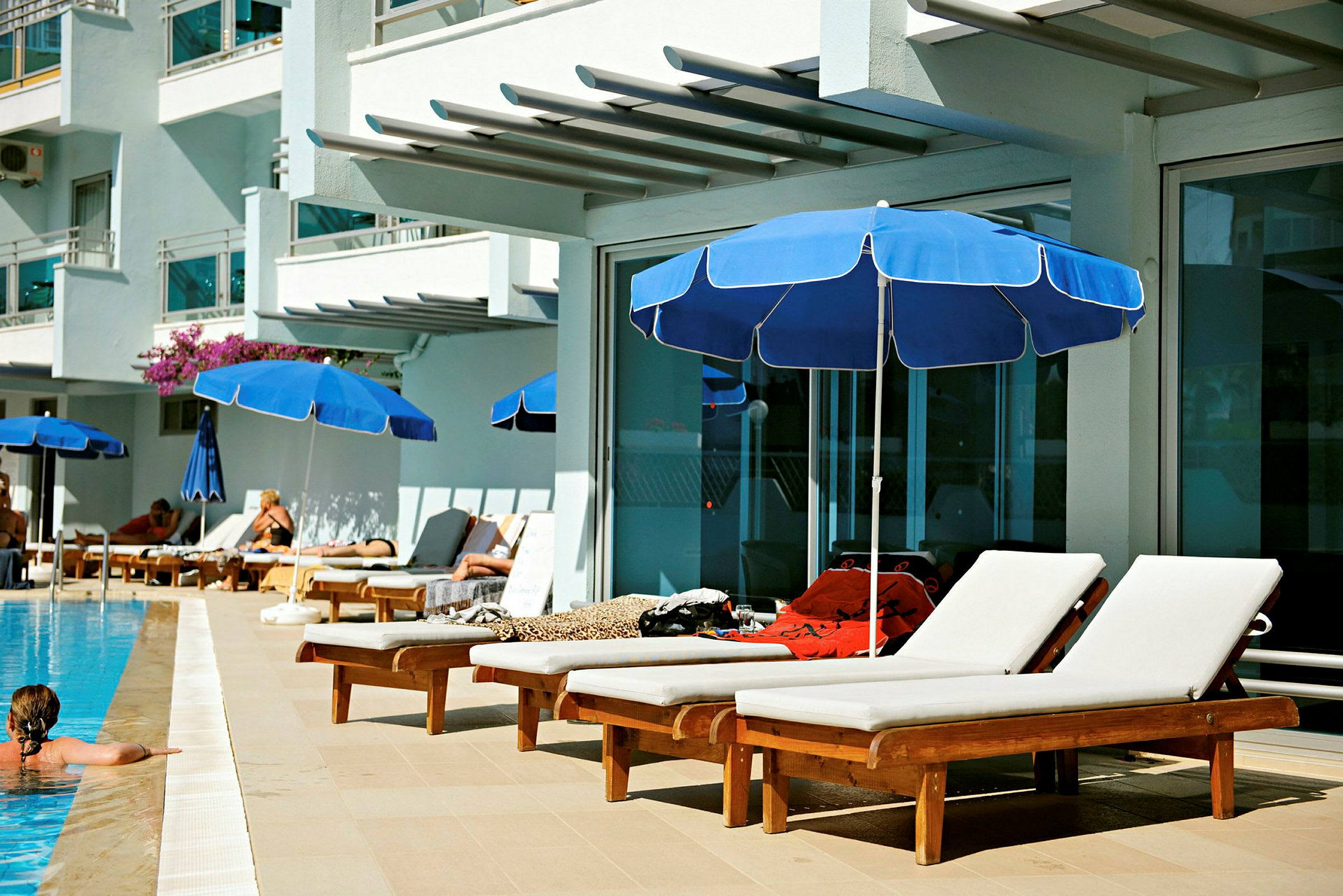 Flera solstolar med blå parasoller vid en pool nära en hotellbyggnad. (AI-genererad text)
