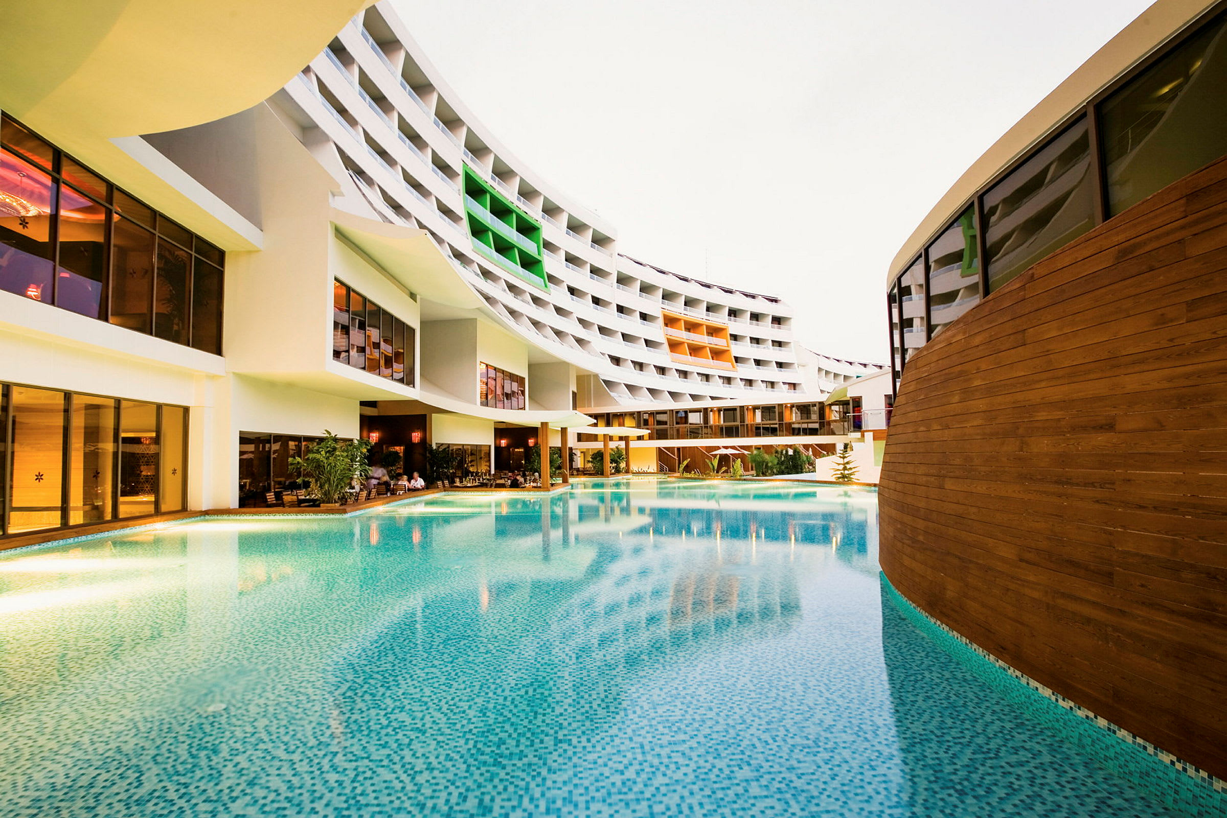 En stor utomhuspool framför ett modernt hotell med färgglada balkonger. (AI-genererad text)