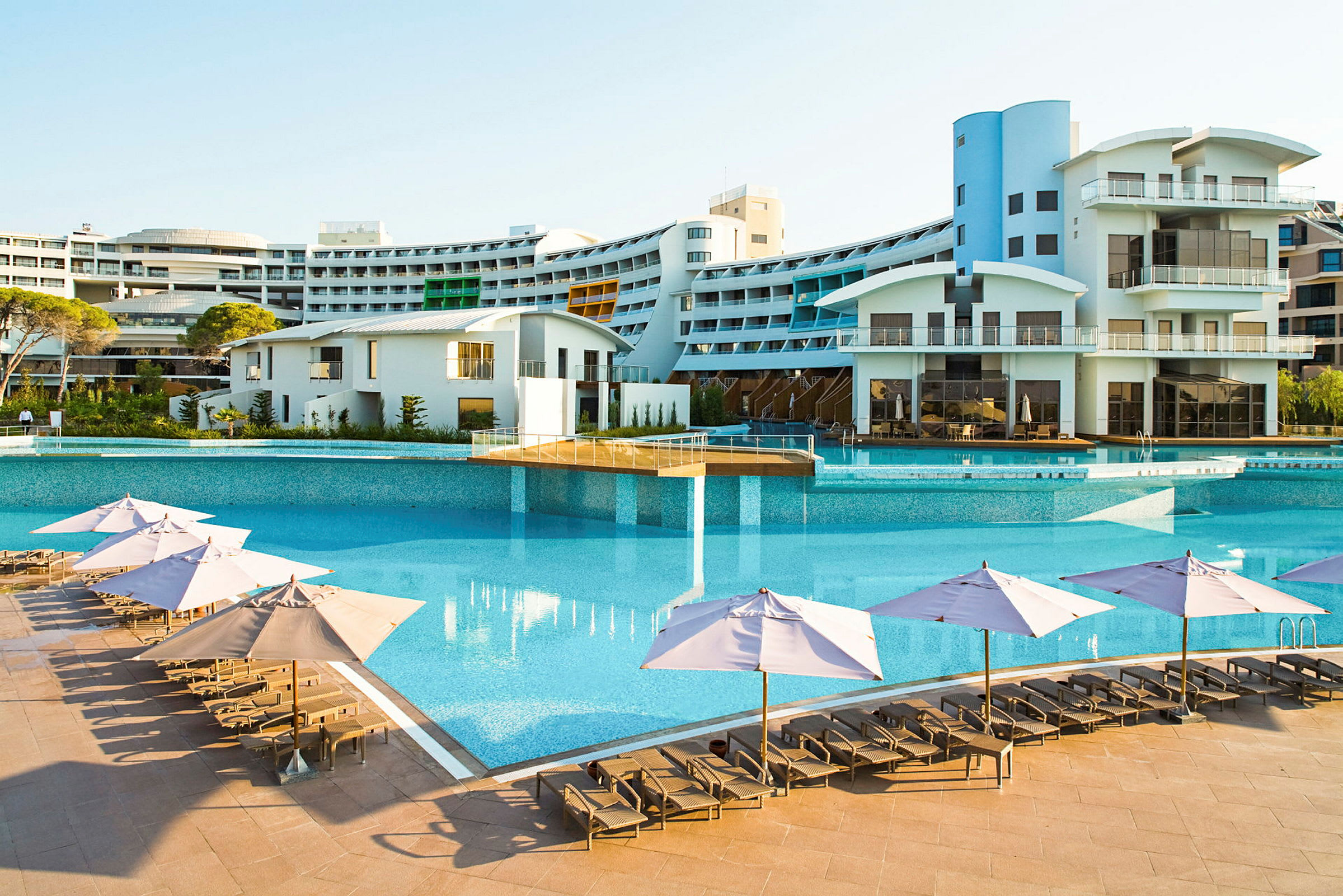 En stor utomhuspool med solstolar och parasoll framför ett modernt hotell. (AI-genererad text)