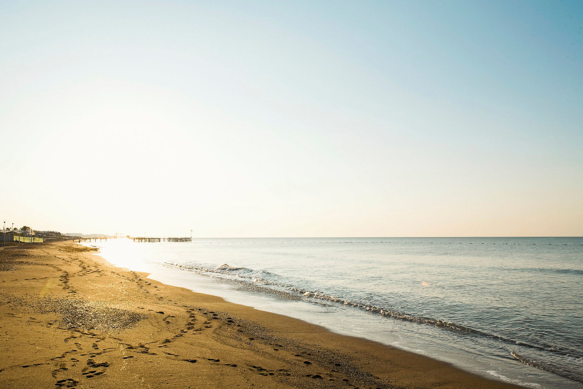 Solnedgång över en sandstrand med havet och en brygga i bakgrunden. (AI-genererad text)