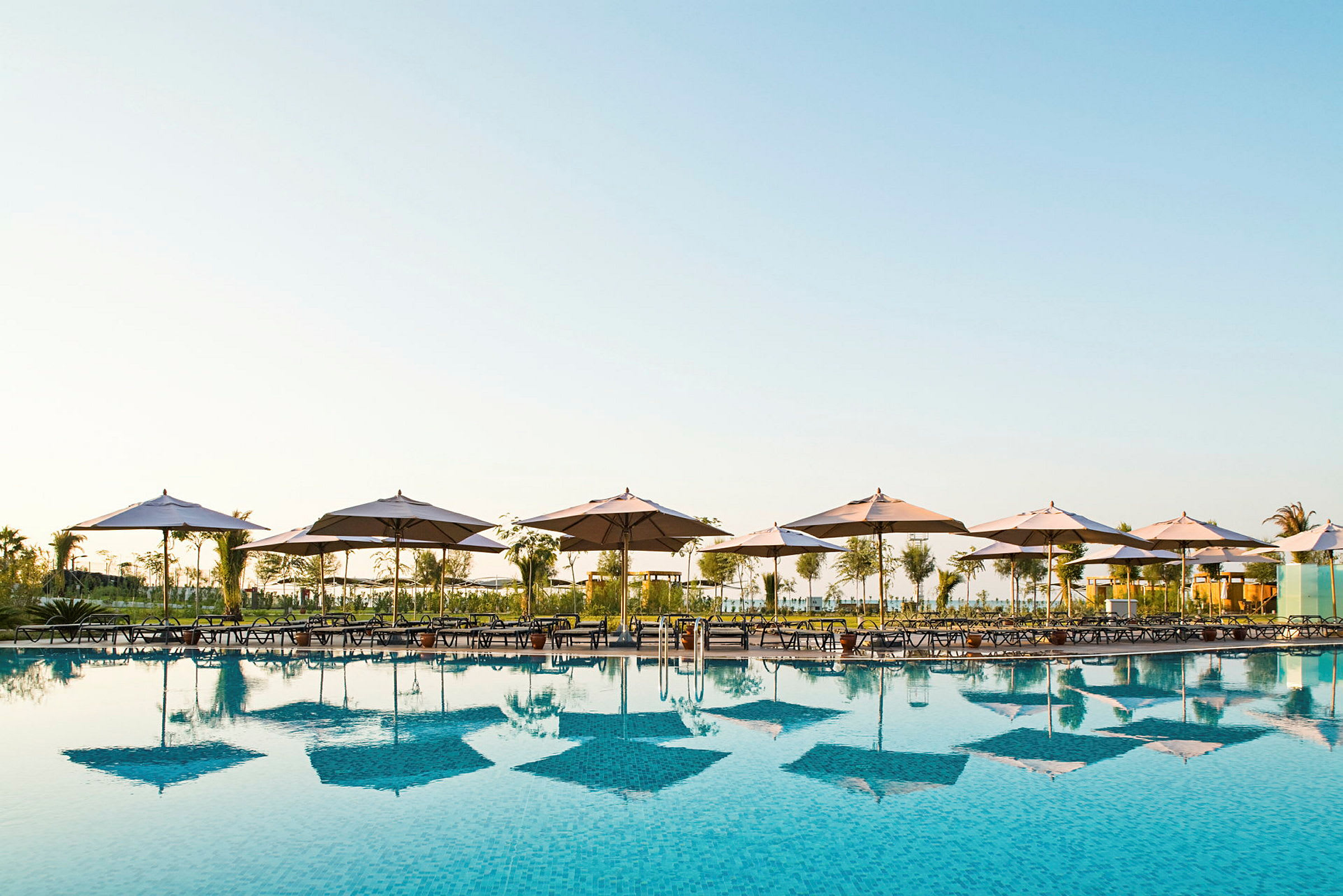 En swimmingpool med solstolar och parasoller vid kanten. (AI-genererad text)