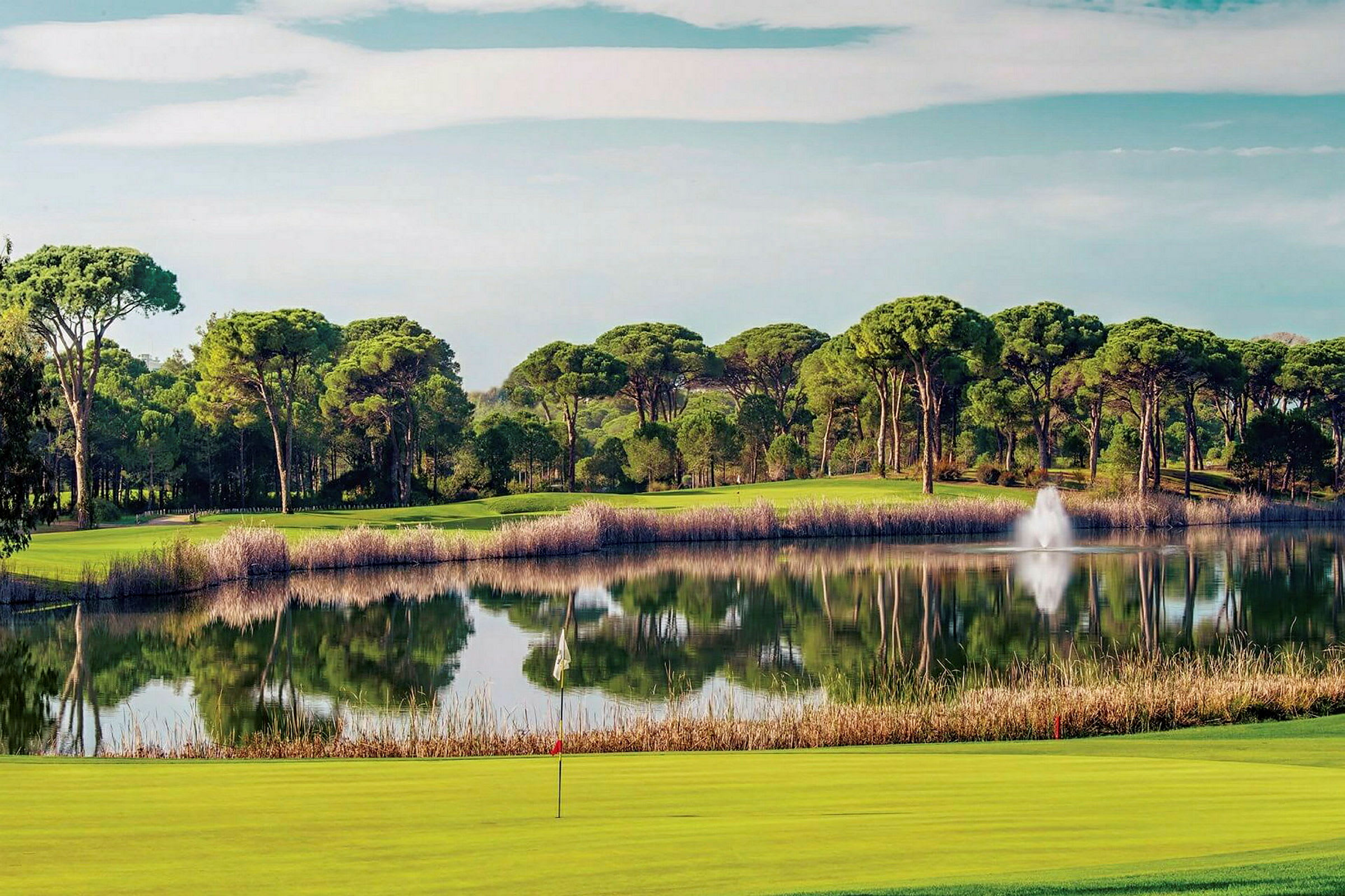Vy över en sjö omgiven av träd med en golfbana i förgrunden. (AI-genererad text)