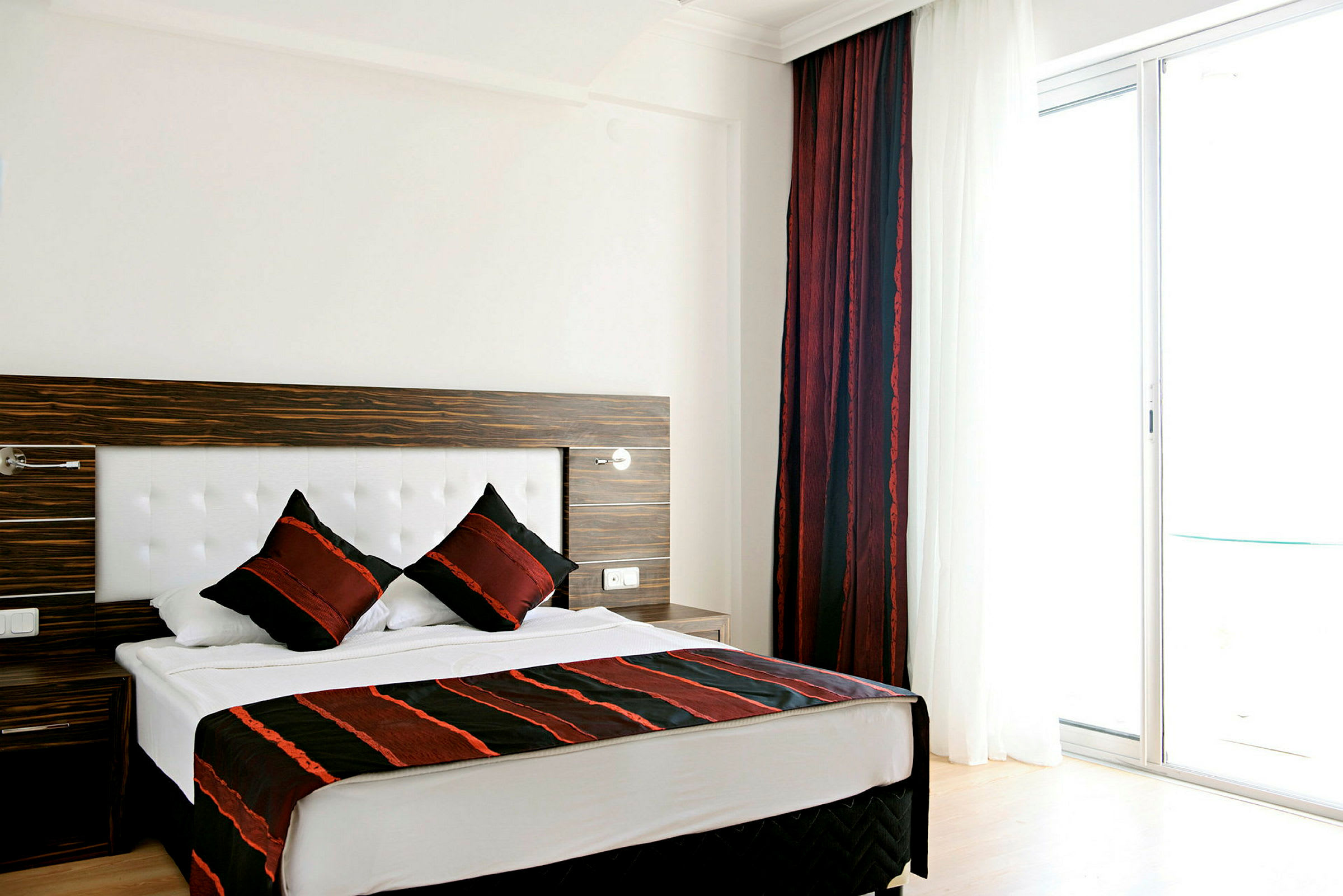 Hotellets rum med en dubbelsäng och röda gardiner vid ett fönster. (AI-genererad text)