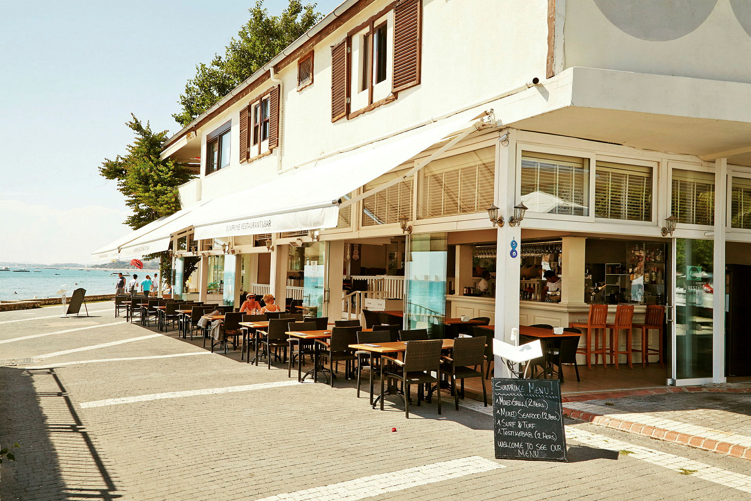 Ett kafé eller restaurang med sittplatser utomhus och utsikt mot havet. (AI-genererad text)