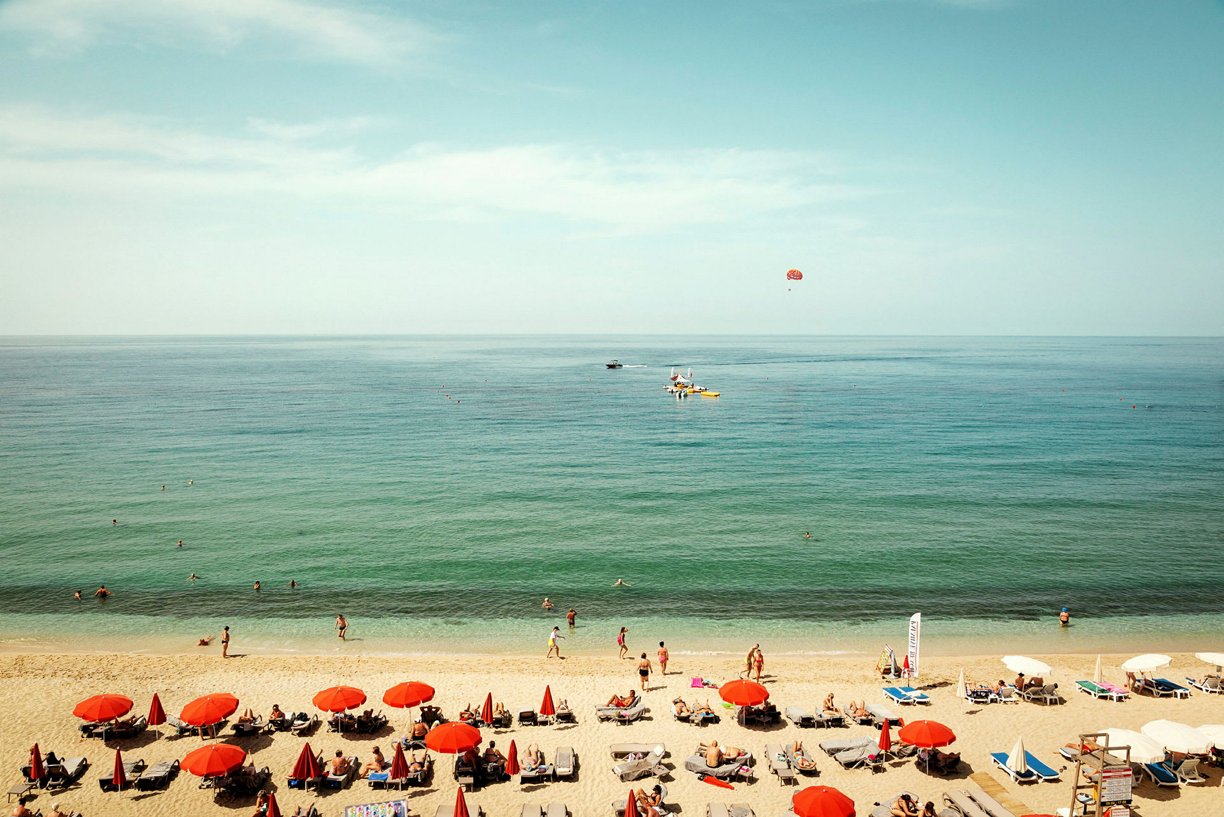 En strandscen med röda parasoller, solstolar och människor vid vattnet. (AI-genererad text)
