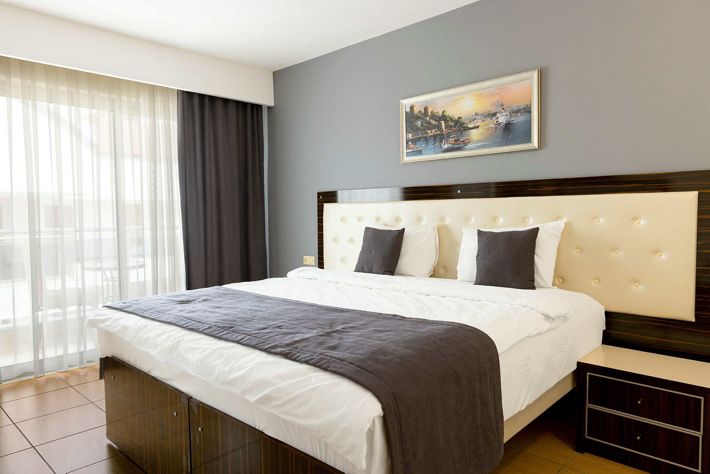Ett modernt hotellrum med en dubbelsäng, en grå sänglampa och en tavla på väggen. (AI-genererad text)