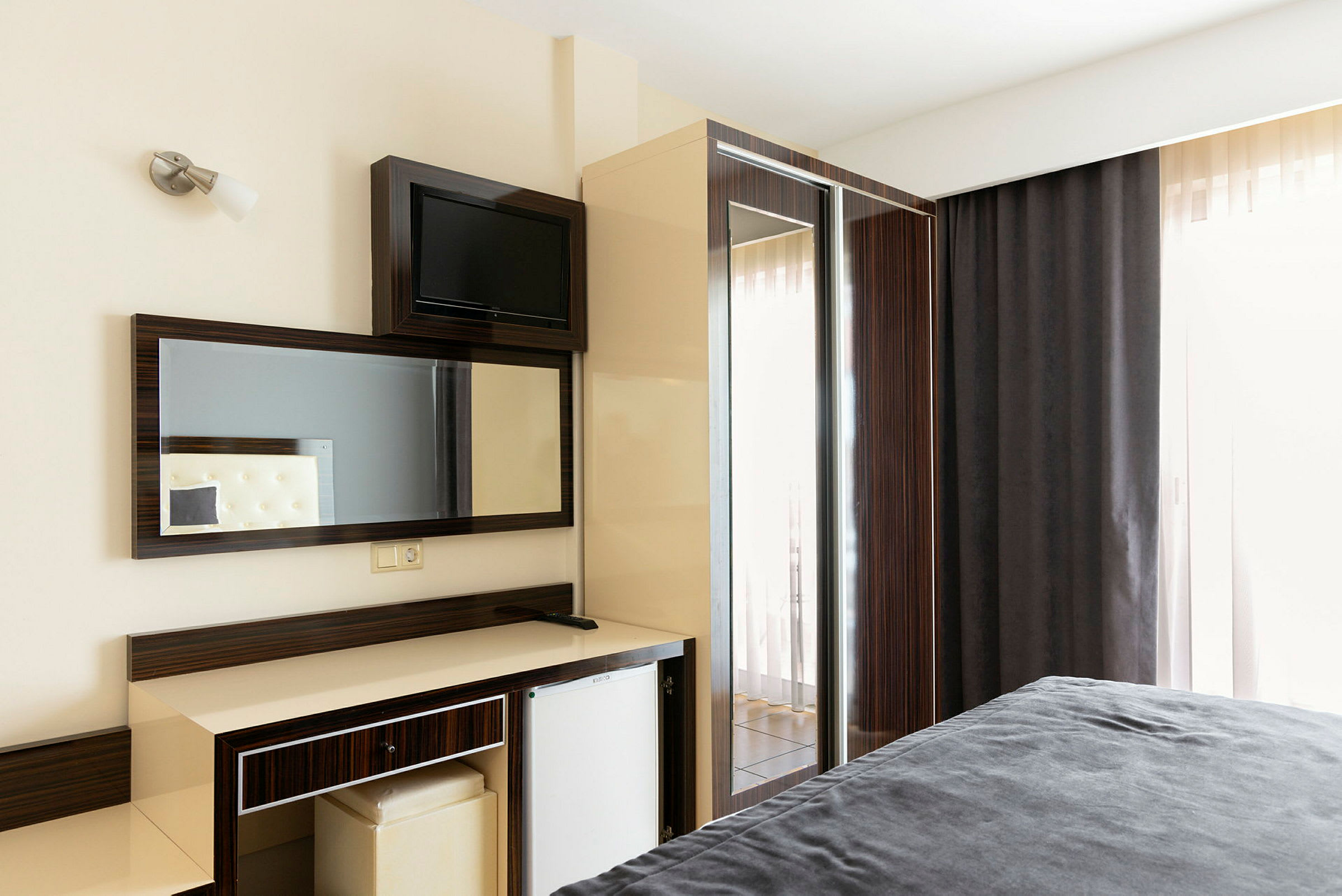 Ett hotellrum med skrivbord, spegel, och ett kylskåp. (AI-genererad text)
