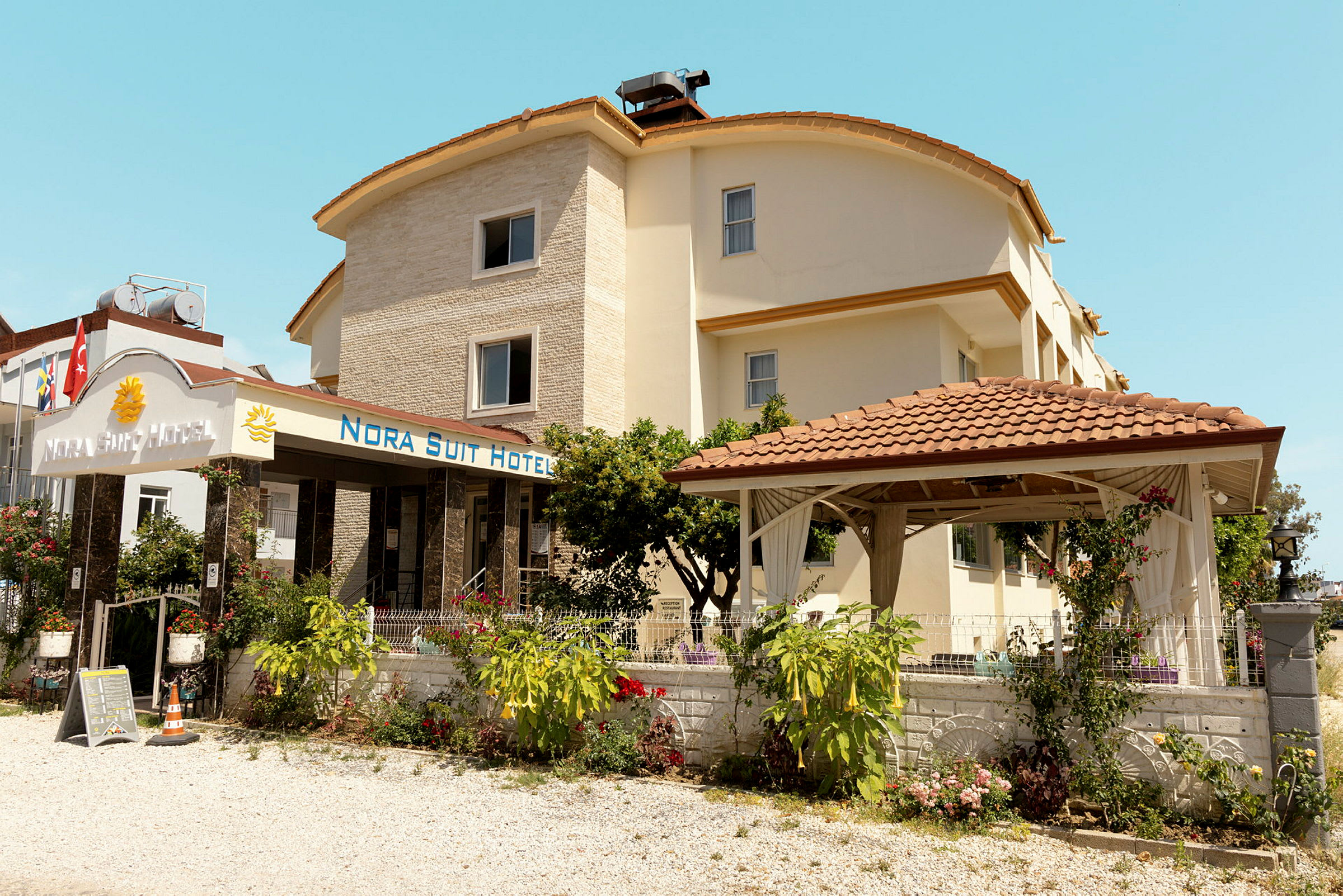Exteriör av Nora Suit Hotel med trädgård och pergola. (AI-genererad text)