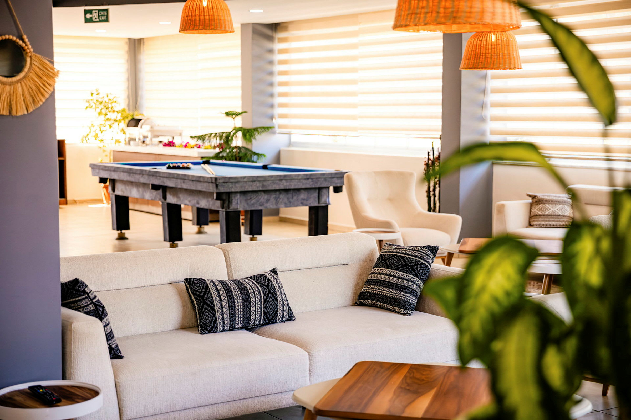 En ljus och stilren lounge med soffor, kuddar och ett biljardbord i bakgrunden. (AI-genererad text)