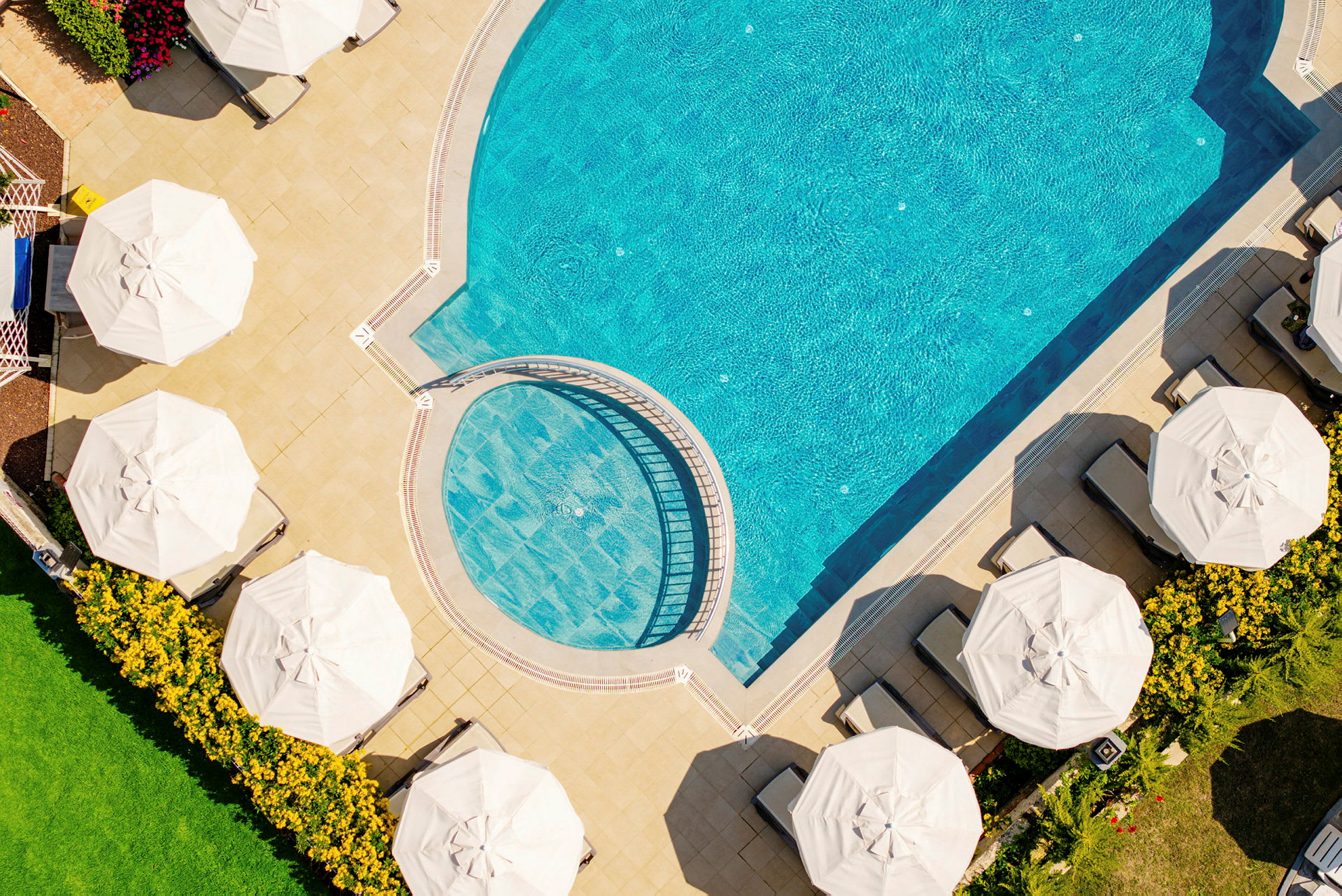 En pool sedd ovanifrån med solstolar och parasoller bredvid. (AI-genererad text)