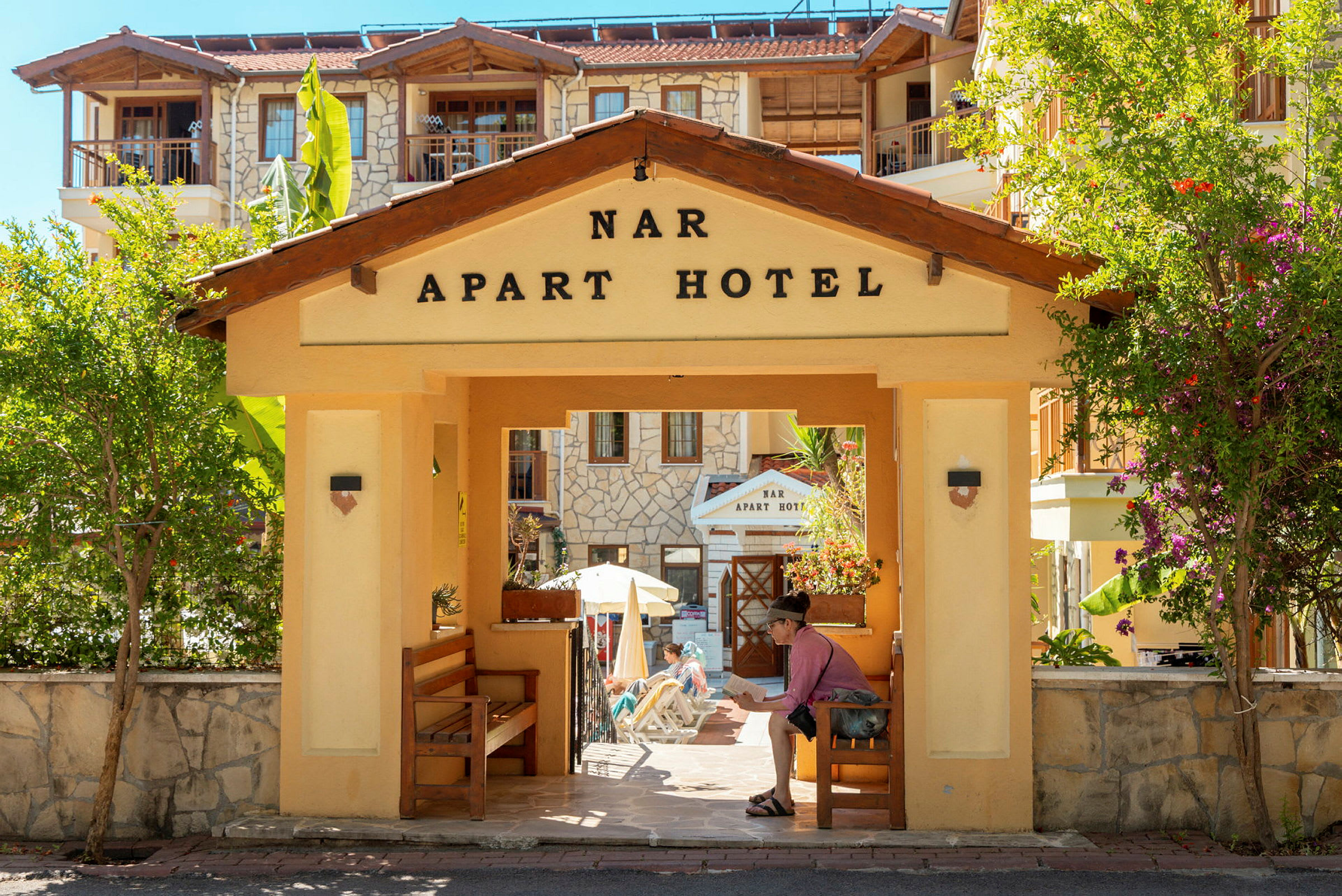 Entré till Nar Apart Hotel med blommor och grönska. (AI-genererad text)