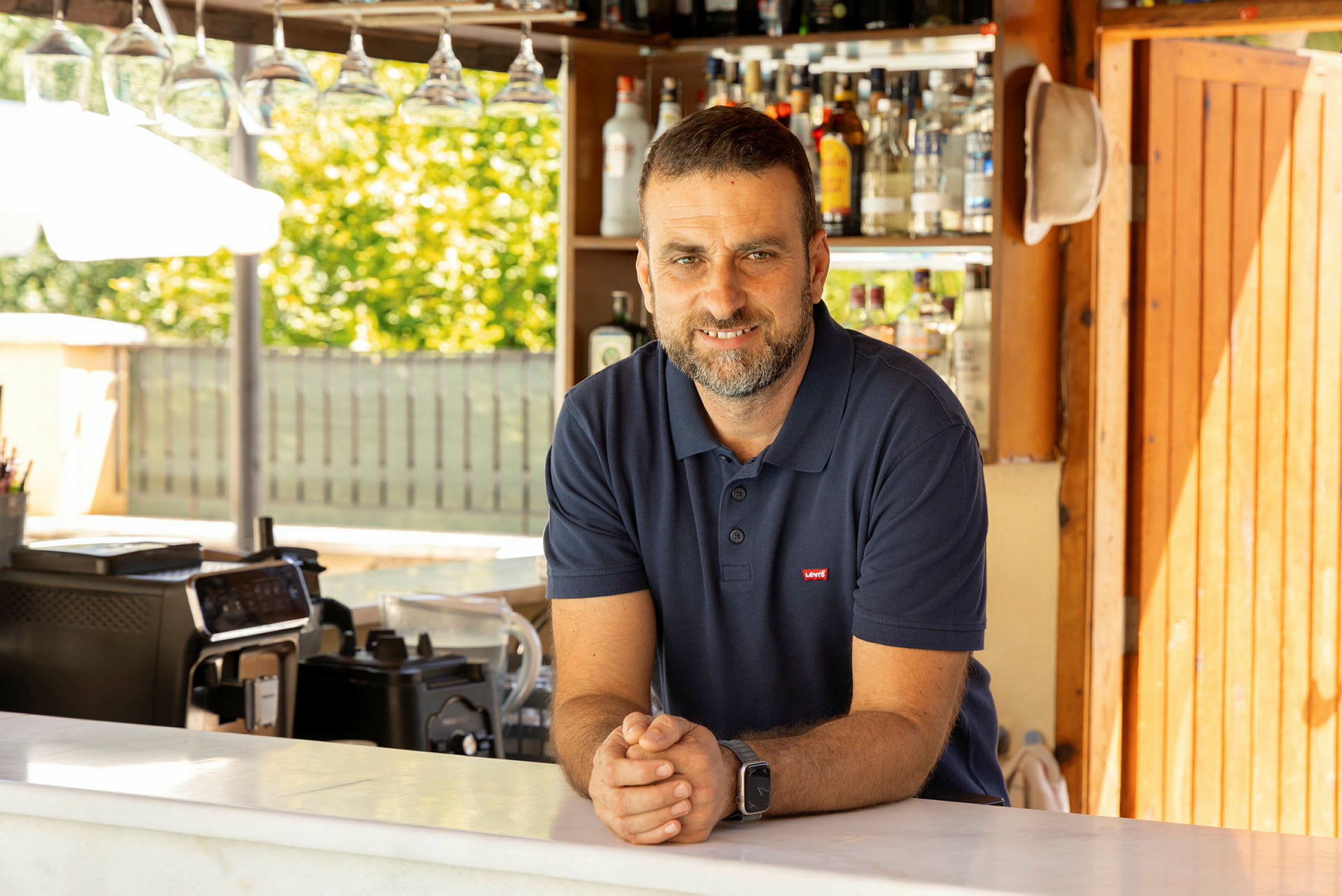 En man står bakom en bar med flaskor i bakgrunden. (AI-genererad text)