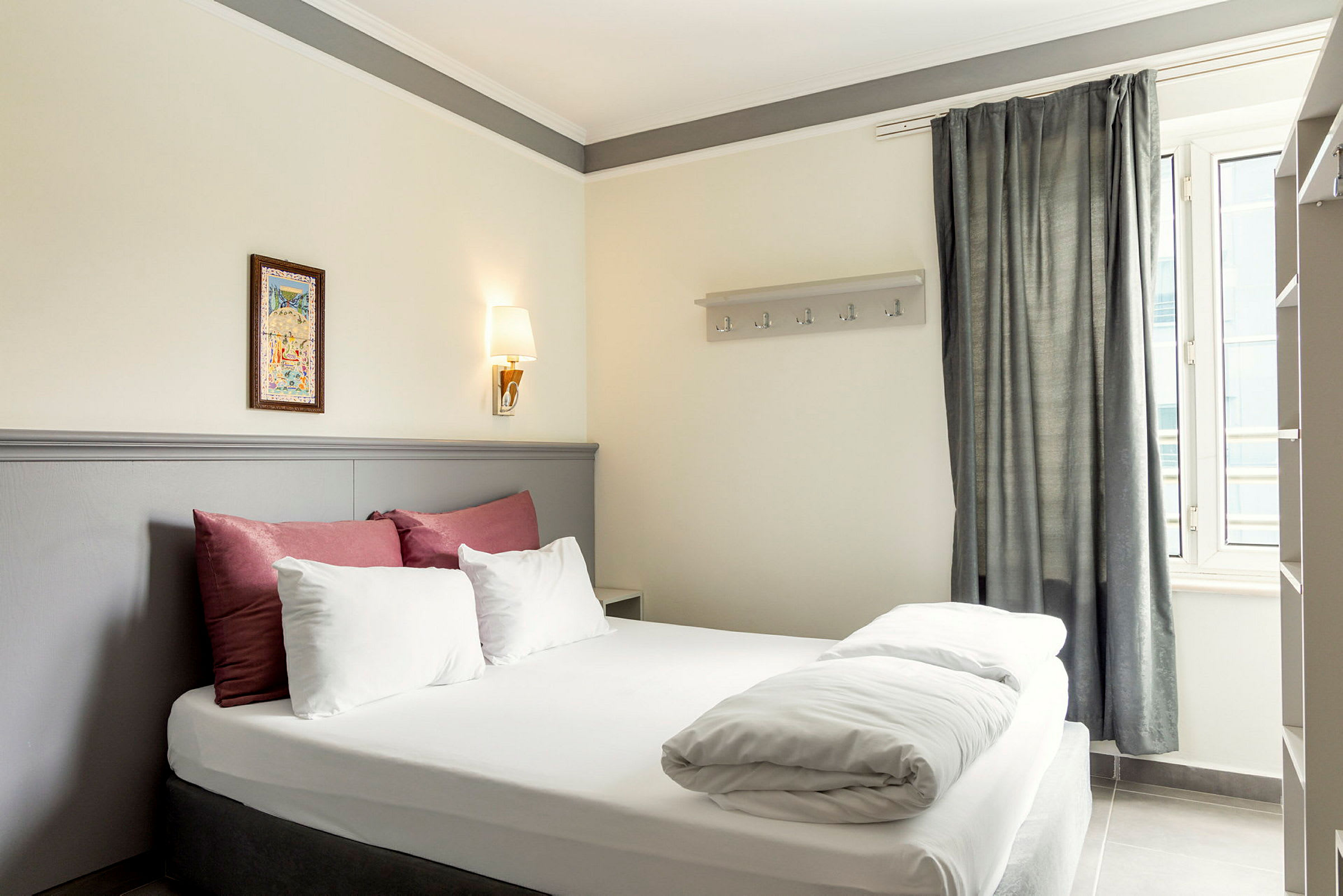 Bild på ett hotellrum med en dubbelsäng, dekorerad med sängkläder i vitt och rött samt en ljusgrå sänggavel. (AI-genererad text)