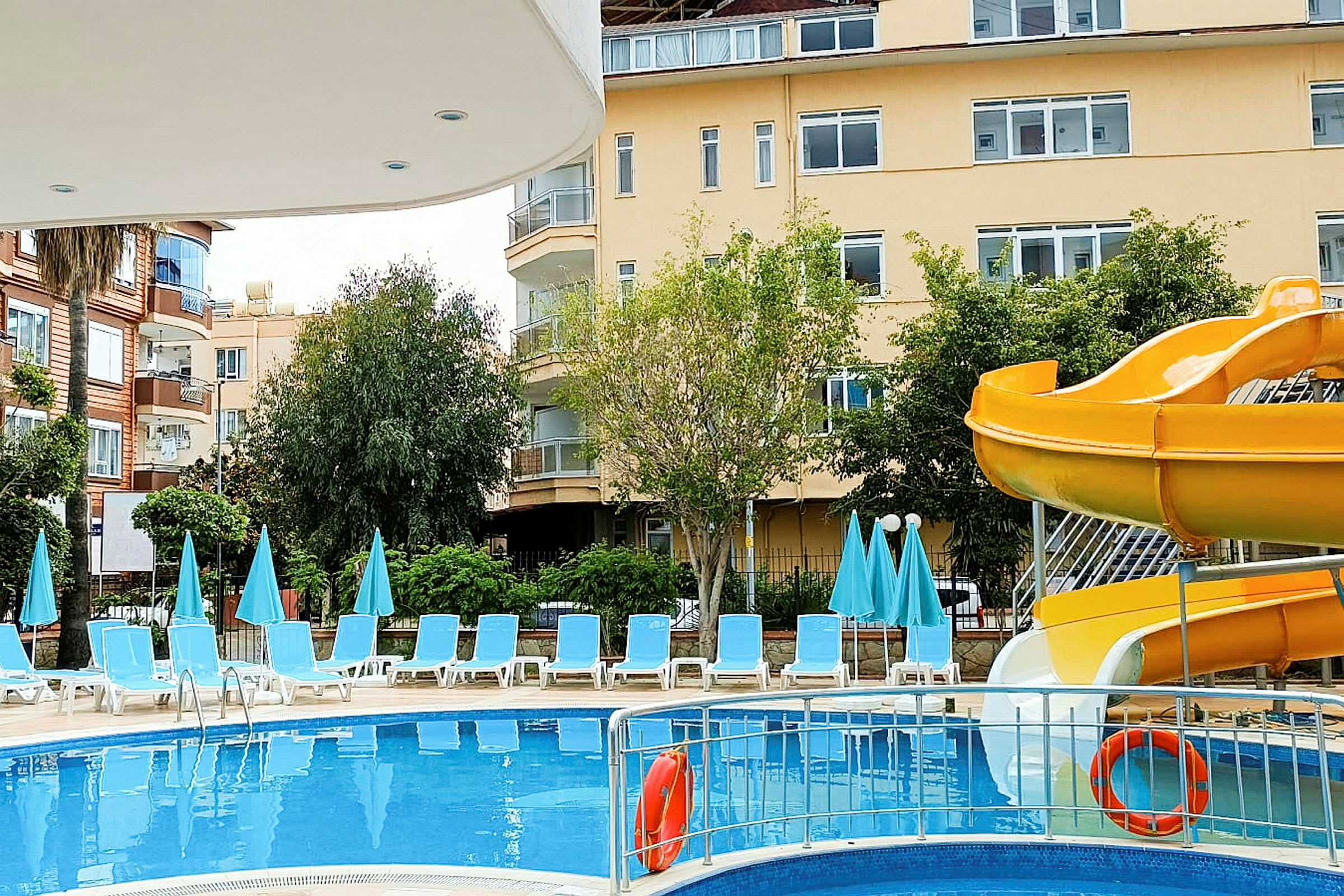 Poolområde med solstolar, parasoller och en gul vattenrutschkana. (AI-genererad text)