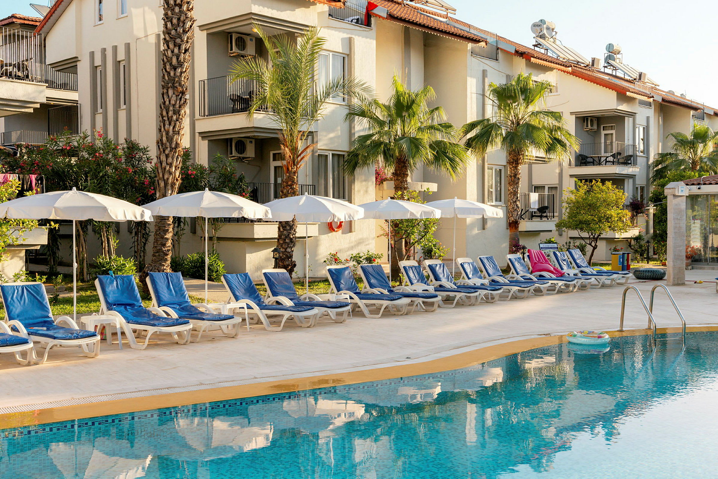 Bild av en pool med solstolar och parasoller framför ett hotell. (AI-genererad text)