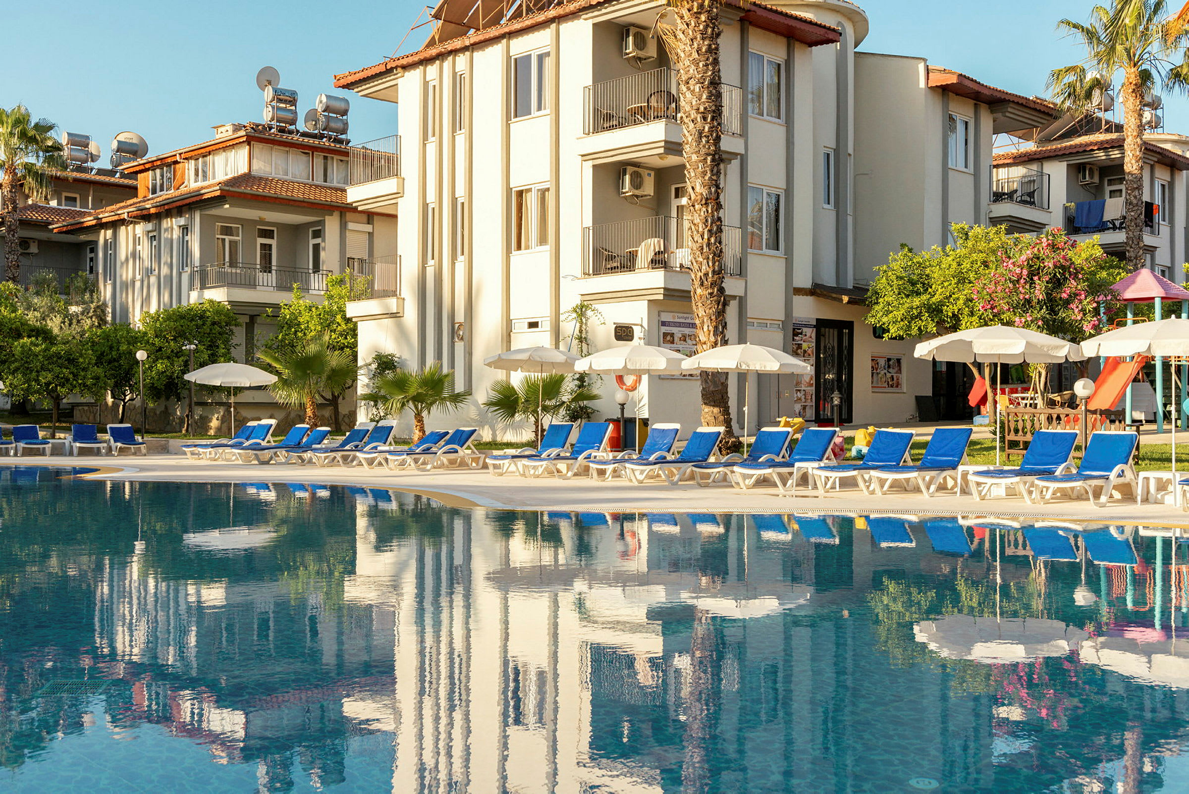 En utomhuspool framför ett hotell med solstolar och parasoller. (AI-genererad text)