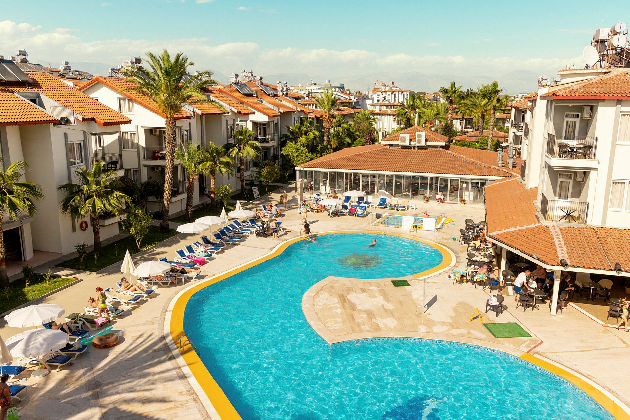 Hotellområde med pool och solstolar omgivna av byggnader med röda tegeltak. (AI-genererad text)