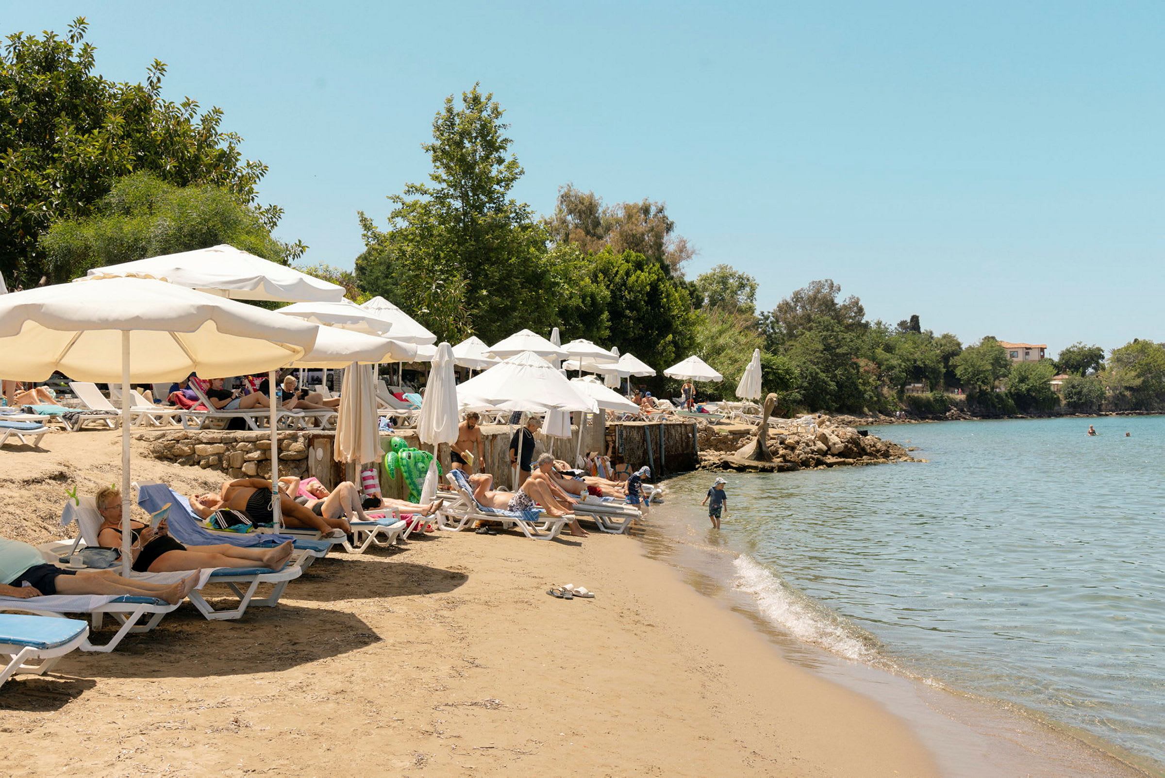 Badstrand med solstolar och parasoll bredvid en strandkant med klart vatten. (AI-genererad text)