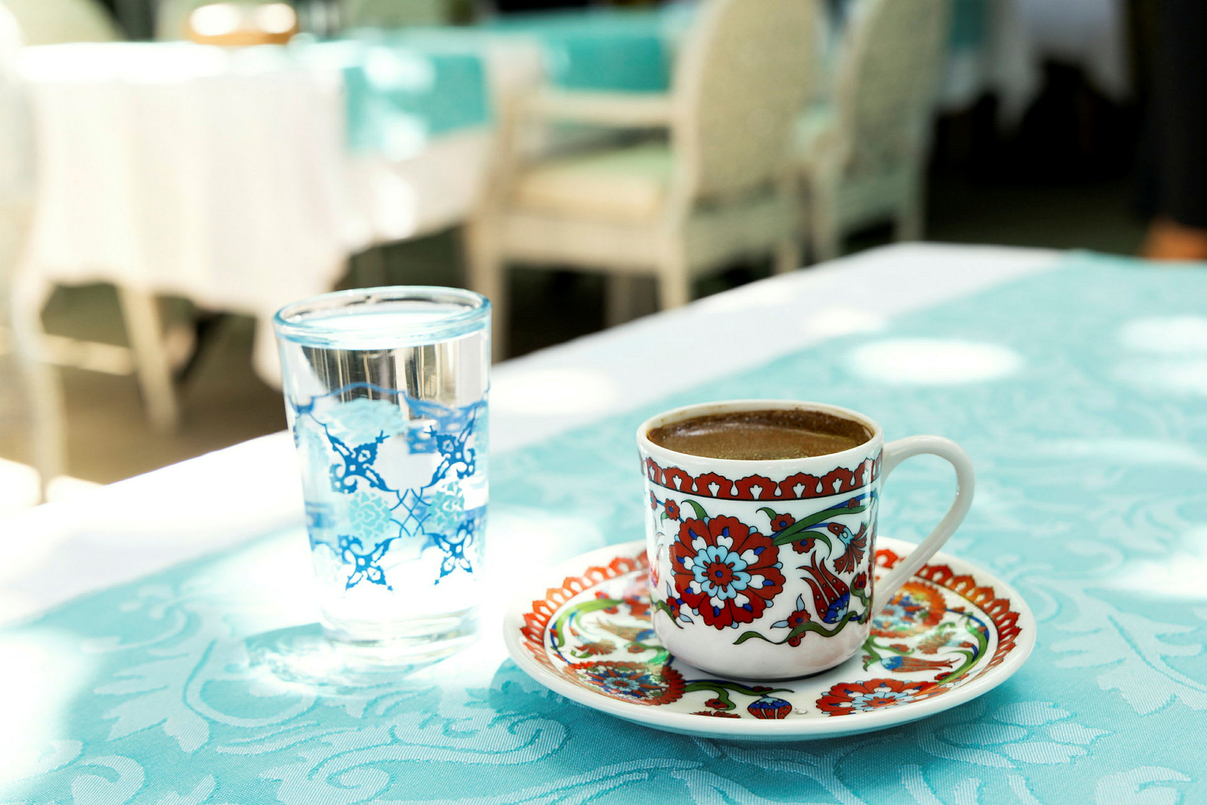 En kopp med färgglatt mönster innehållande kaffe bredvid ett glas vatten på ett bord. (AI-genererad text)