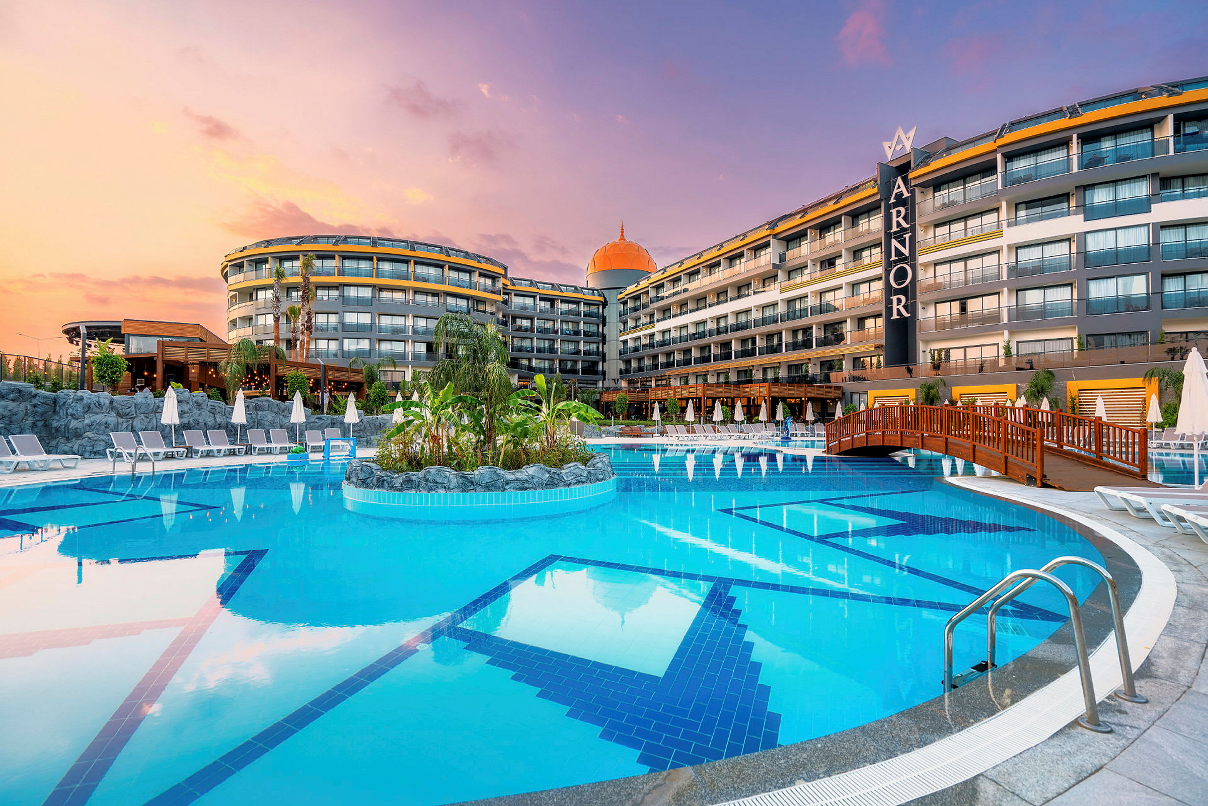 En bild av ett hotell med en stor pool, solstolar runtom och en solnedgång i bakgrunden. (AI-genererad text)