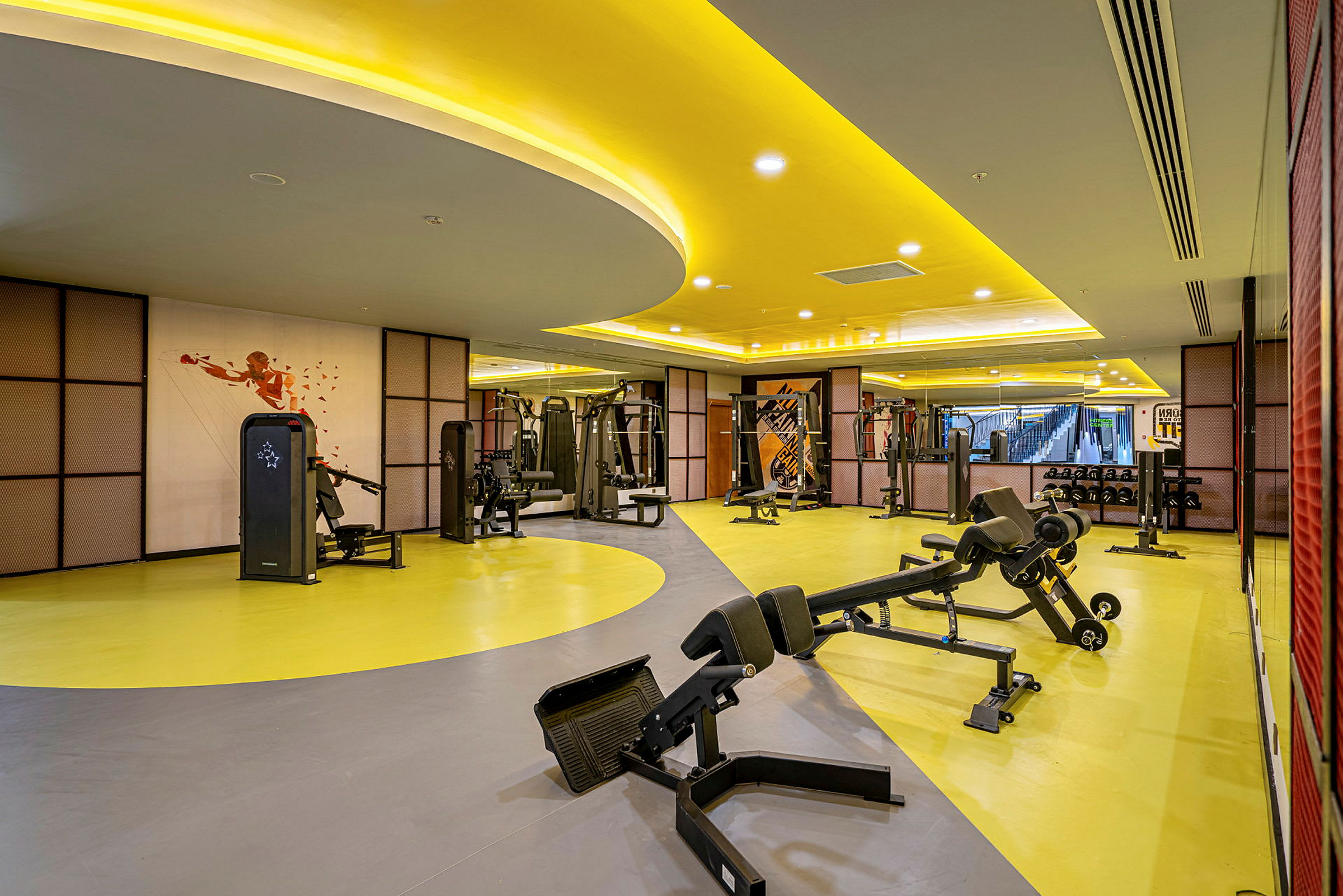 Ett gym med träningsmaskiner och sittande bänkar på ett gulgrått golv. (AI-genererad text)