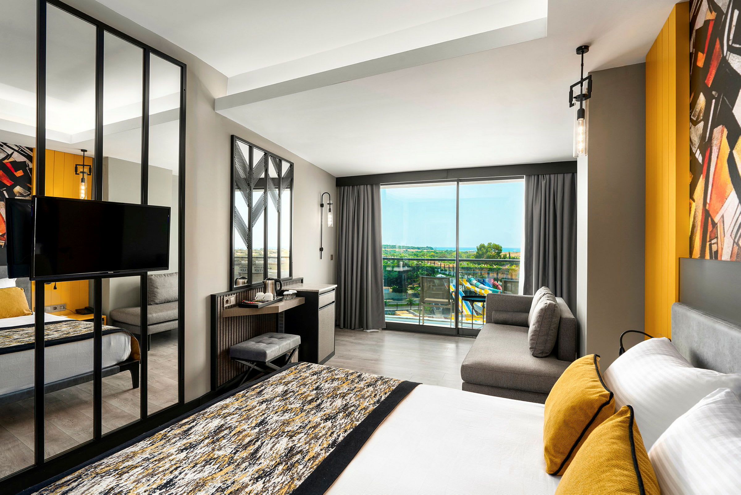 Modernt hotellrum med säng, soffa och utsikt mot balkong med panoramavy. (AI-genererad text)