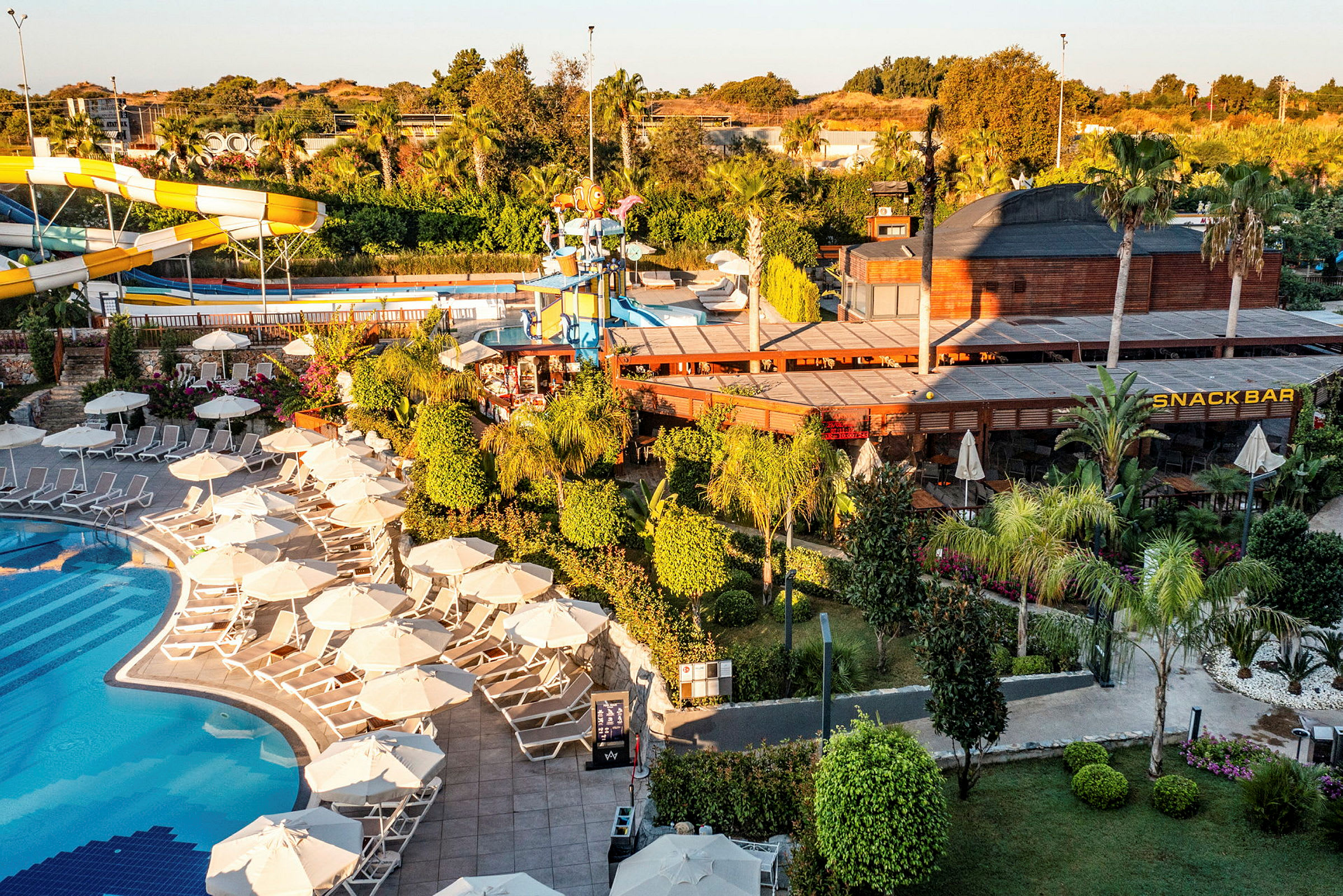 Bild av en resort med pool, solstolar och parasoller, samt en snackbar och vattenrutschbanor. (AI-genererad text)