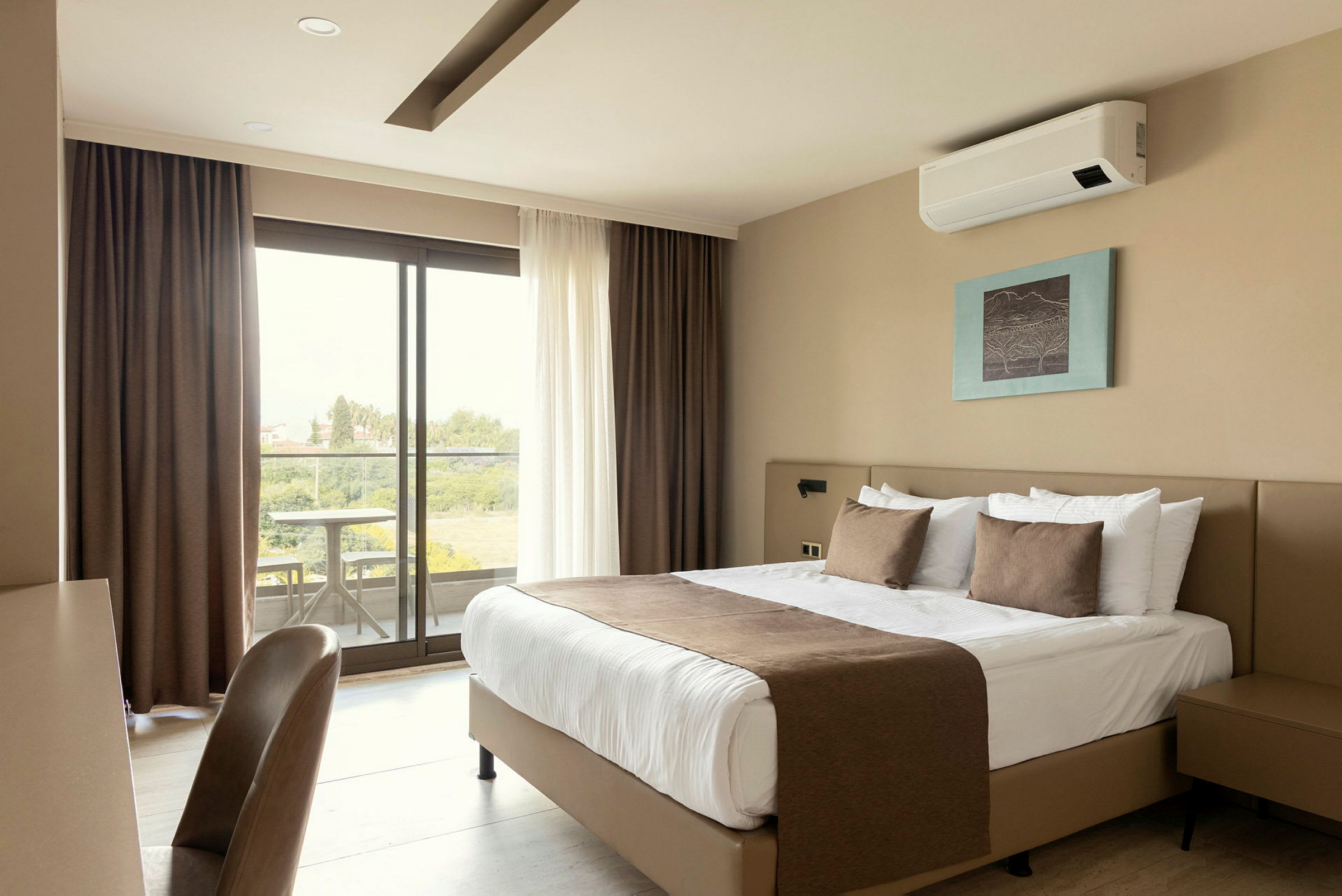Ett hotellrum med en dubbelsäng, en tavla på väggen, ett skrivbord med stol och ett fönster som leder till en balkong med utsikt. (AI-genererad text)