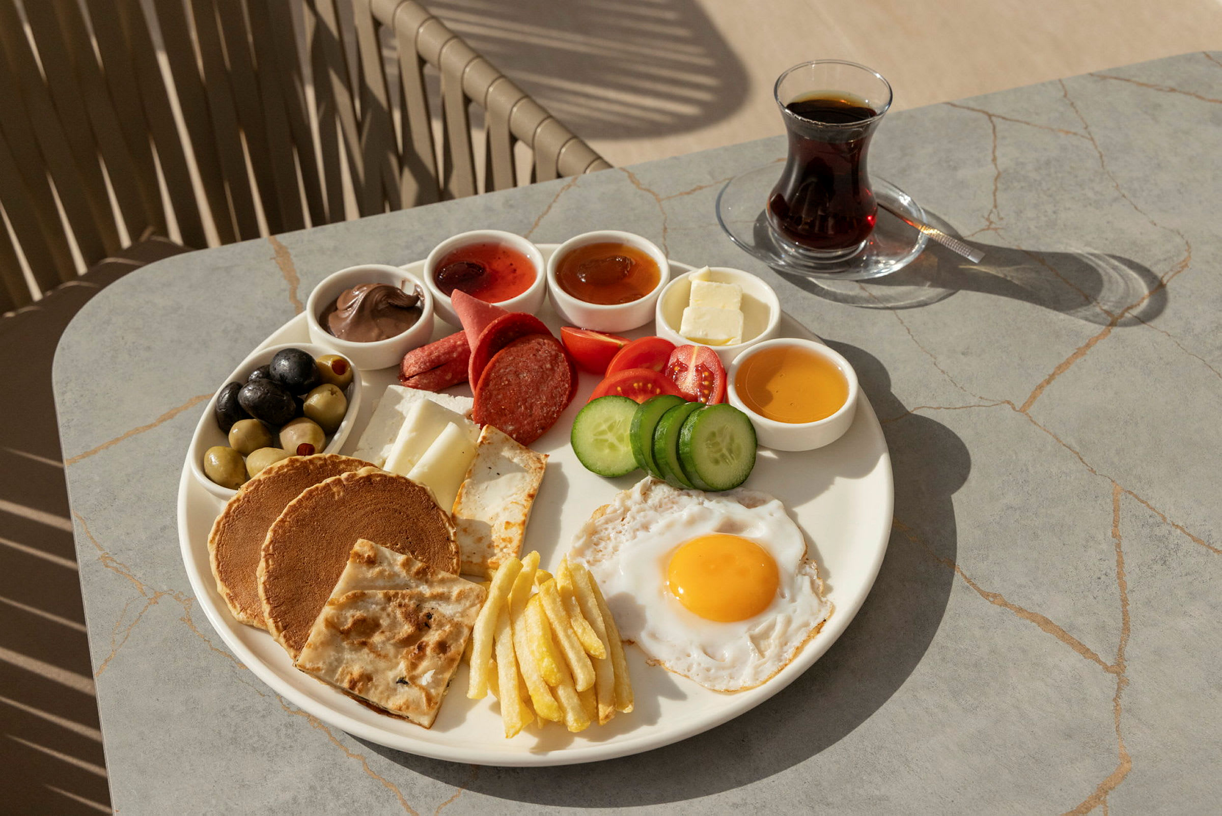 En tallrik med frukostmat som innehåller bland annat ett stekt ägg, grönsaker, bröd och små skålar med olika tillbehör. Bredvid står ett glas te. (AI-genererad text)