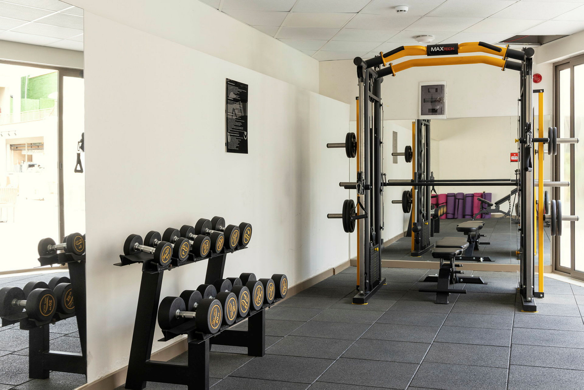 Bild av ett gym med en skivstångsställning och en hylla med hantlar vid sidan. (AI-genererad text)