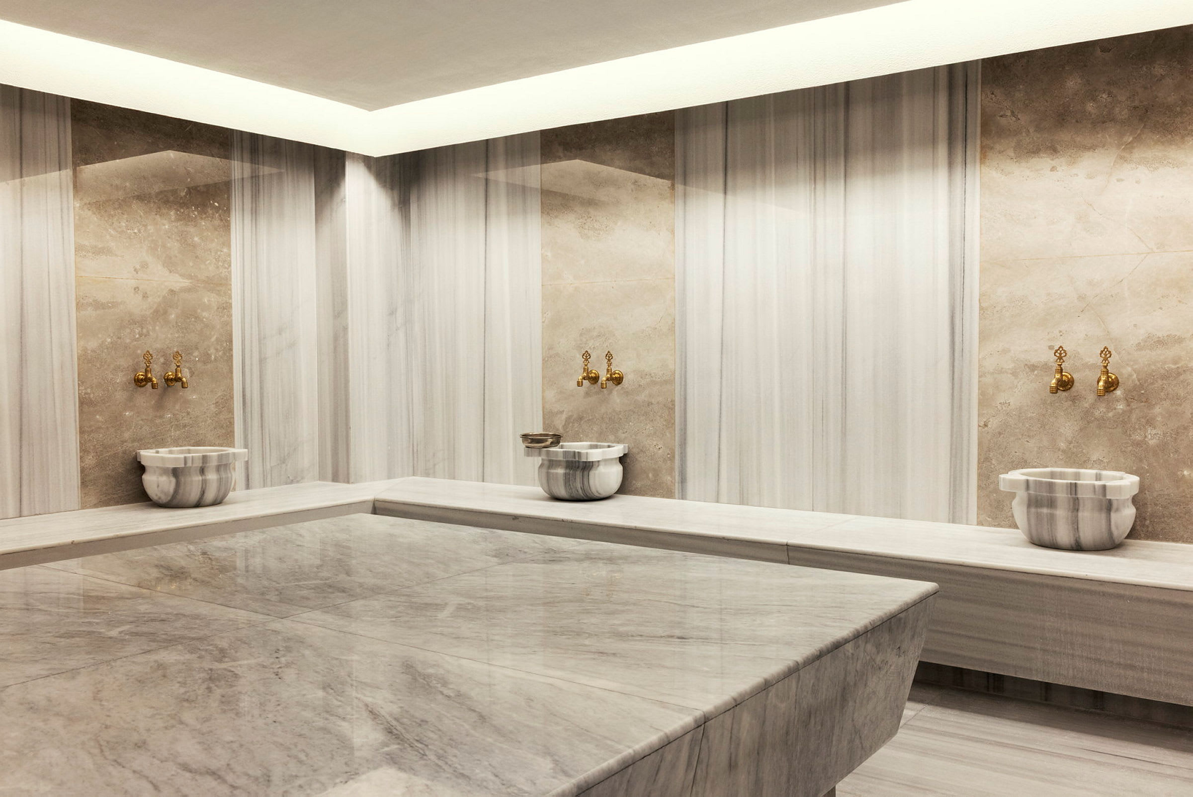 Bild av ett traditionellt turkiskt hamam med marmorytor, vask och kranar. (AI-genererad text)